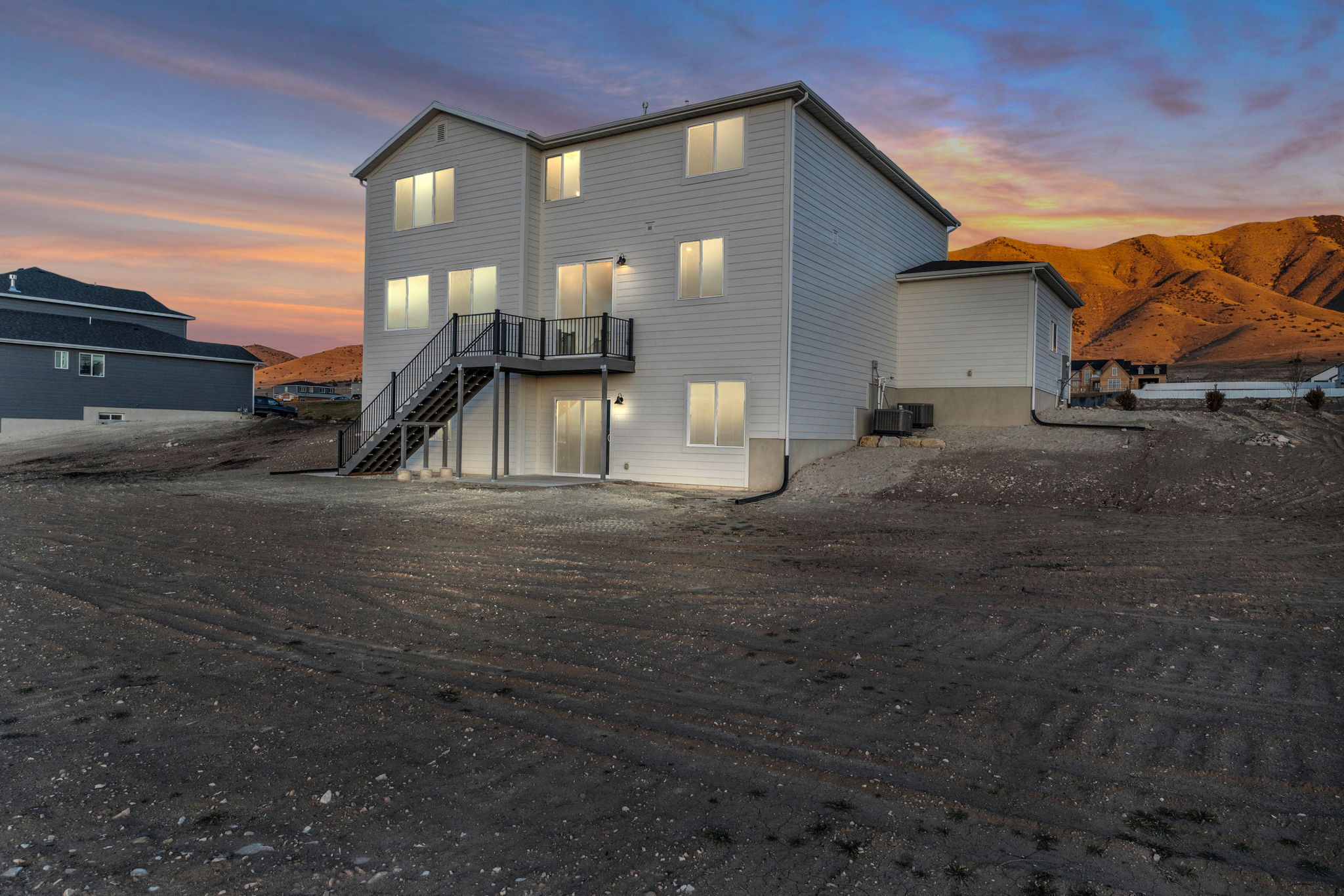 Our two-story "Magnolia" featuring a multi-level deck with dark railings, a ground-level patio door, and multiple windows across three stories.  Nearly flat back yard of the .75 acre lot taken from the southwest corner of property.