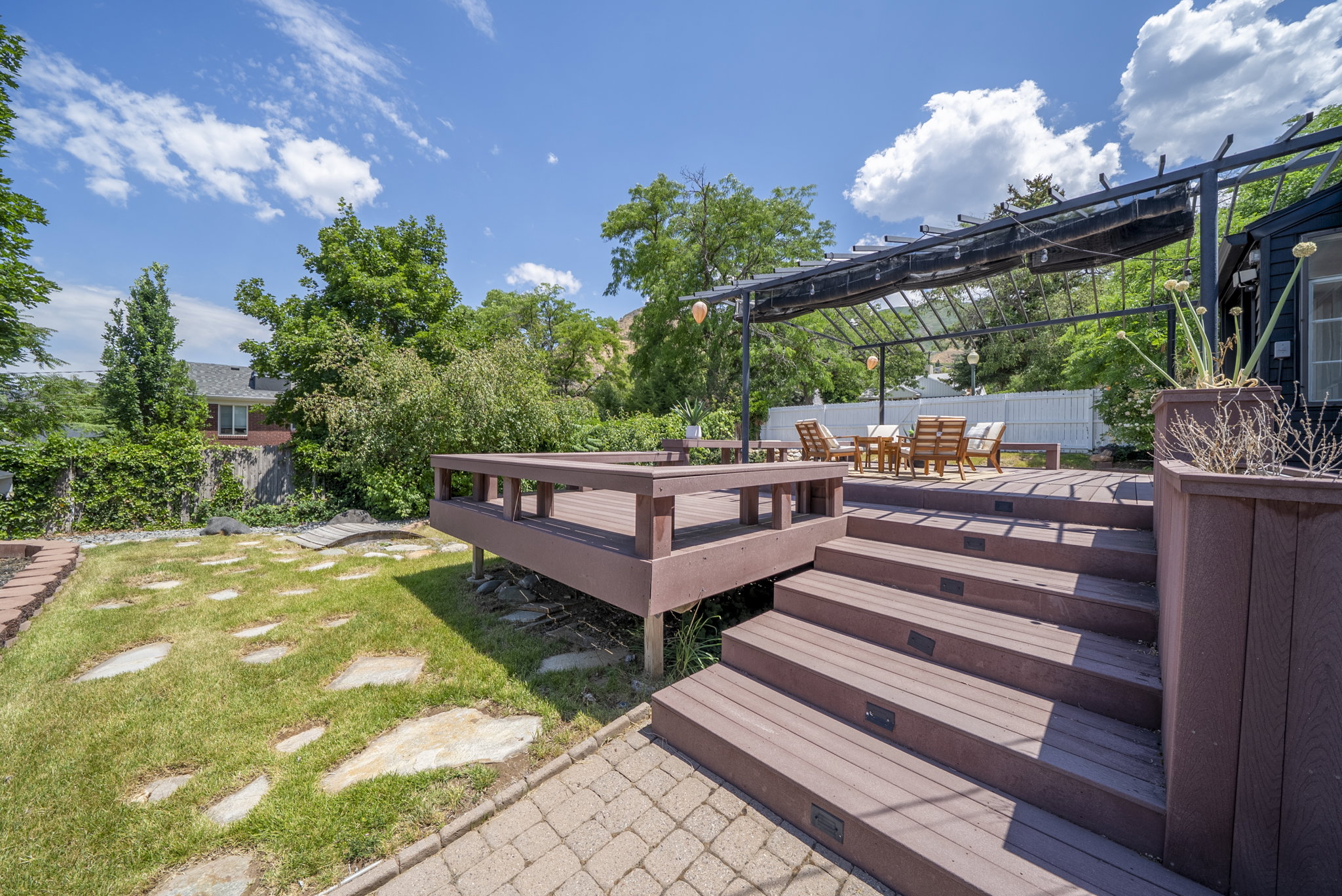 Multi-level outdoor deck featuring integrated steps with lighting, a shaded pergola, and composite decking materials