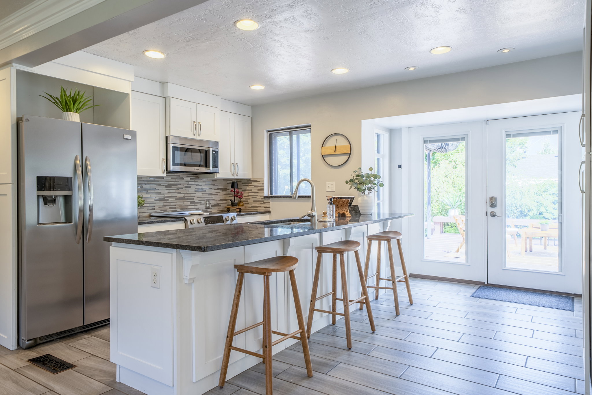 Kitchen featuring white shaker cabinetry, stainless steel appliances, a dark granite countertop island with seating, mosaic tile backsplash, and light wood-finish flooring