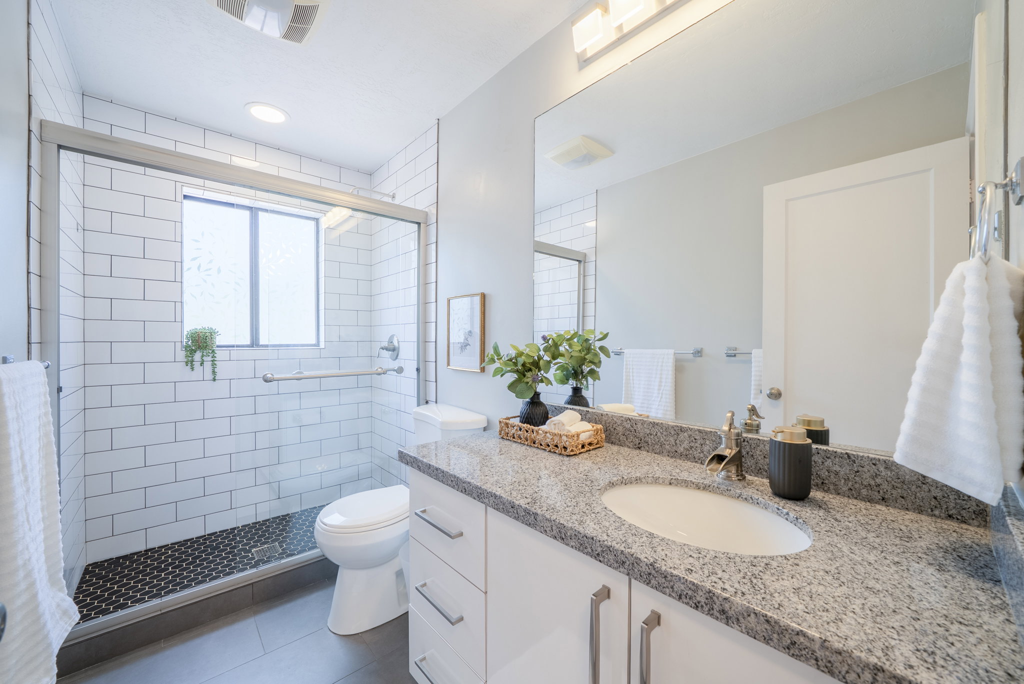 Bathroom featuring a glass-enclosed shower with white subway tile surround and a textured black tile floor