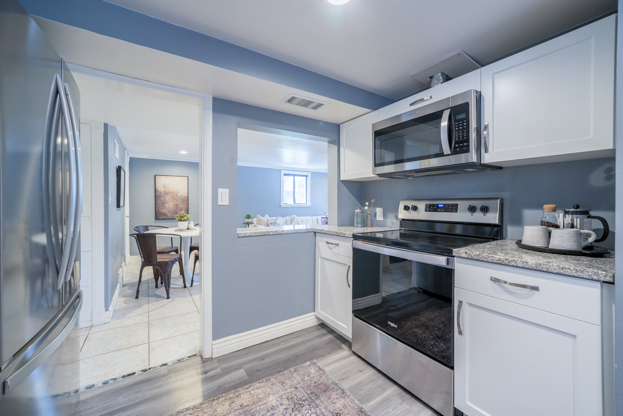 Kitchen featuring white cabinetry, stainless steel appliances, granite-style countertops, and wood-finish flooring
