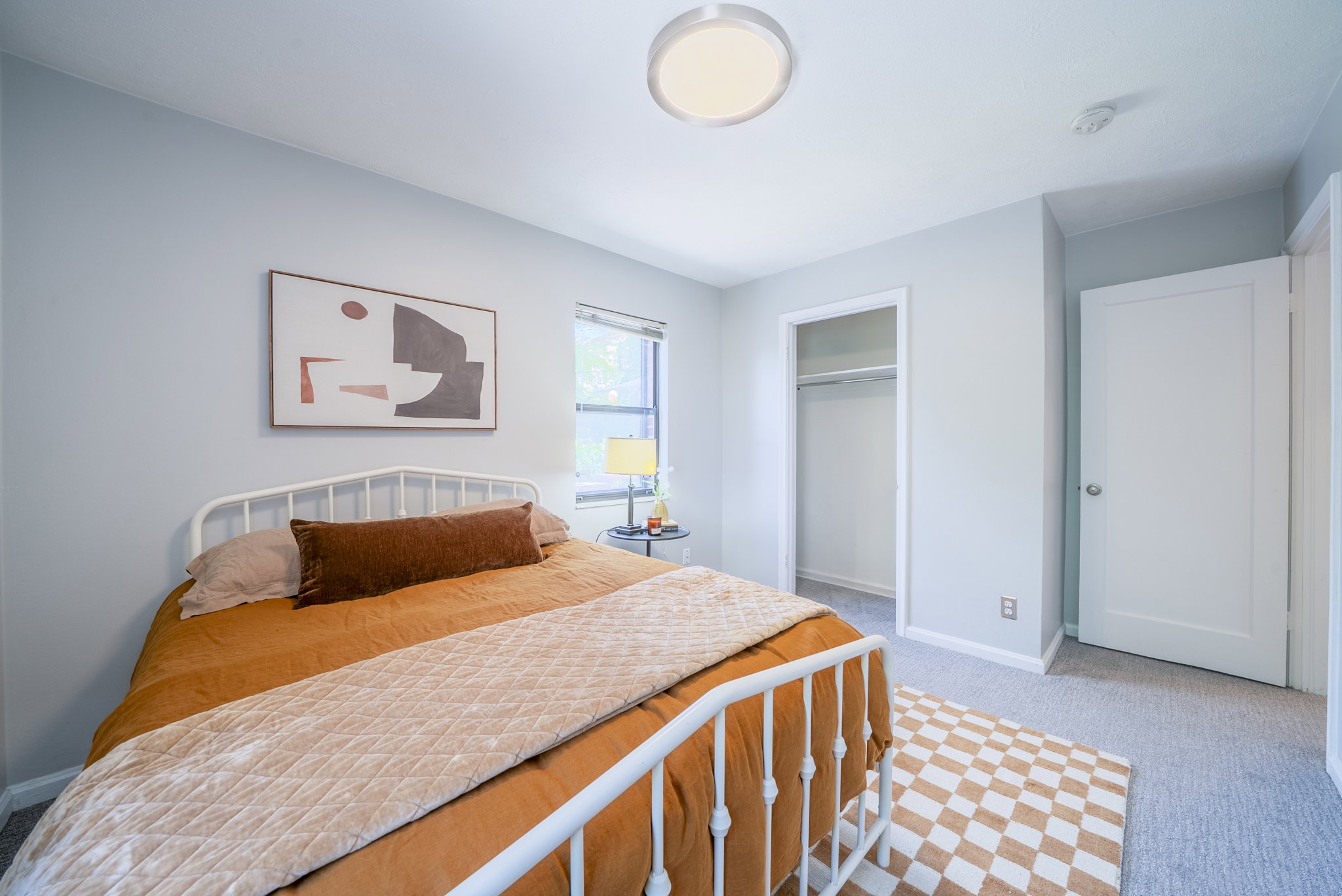 Room with light gray walls, a window with a blind, an open closet with a hanging rod, a white interior door, and a flush-mount ceiling light