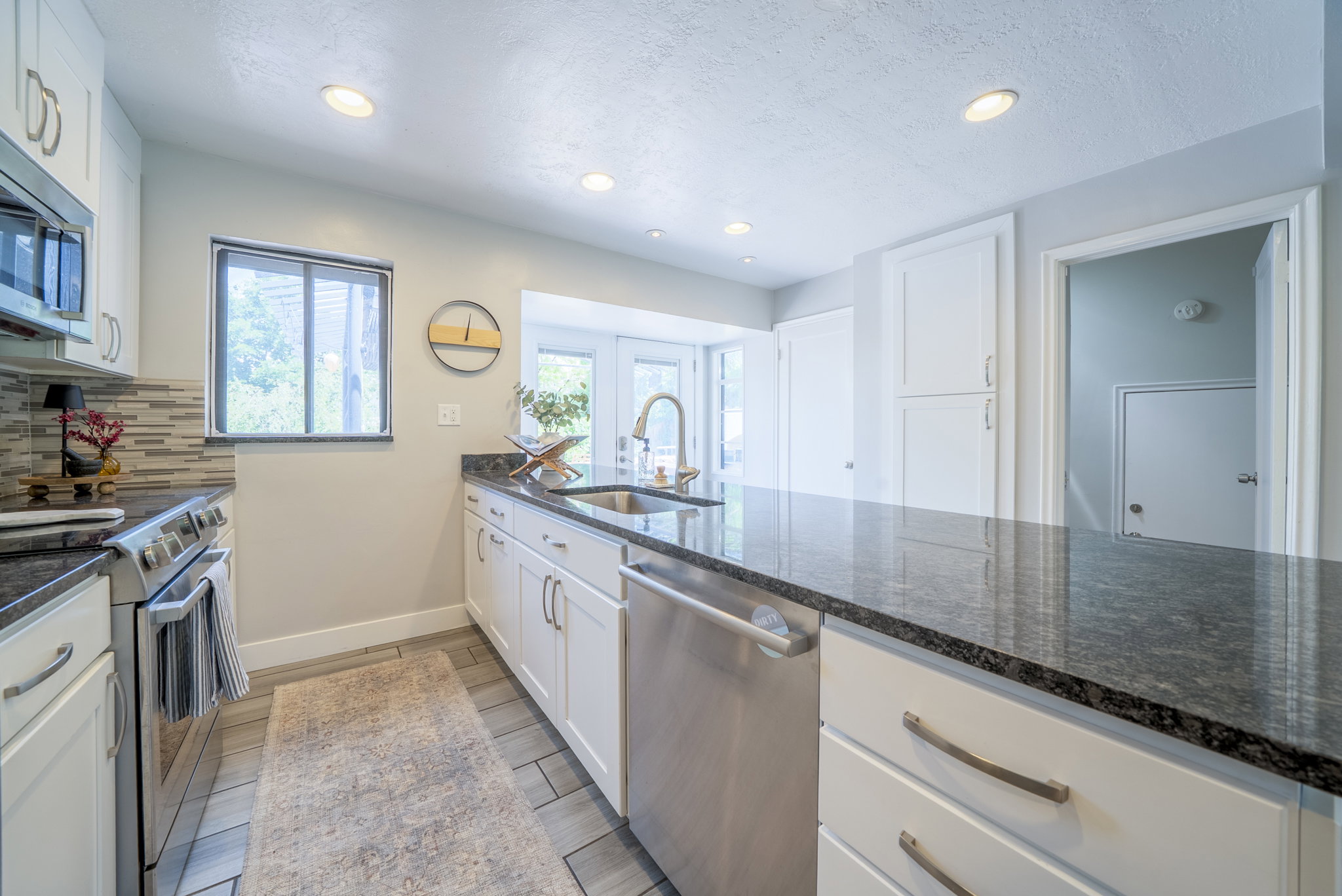 Kitchen featuring dark speckled countertops, white shaker cabinetry, stainless steel appliances, and wood-finish tile flooring
