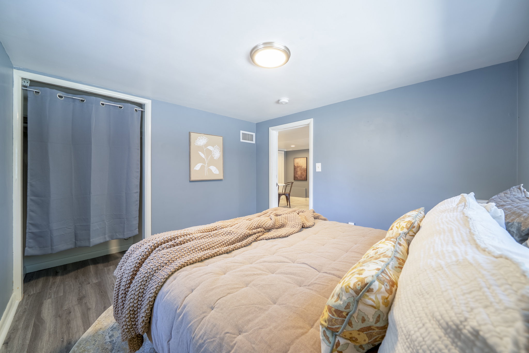 Bedroom featuring light blue walls, wood-finish flooring, and a flush-mount ceiling light fixture