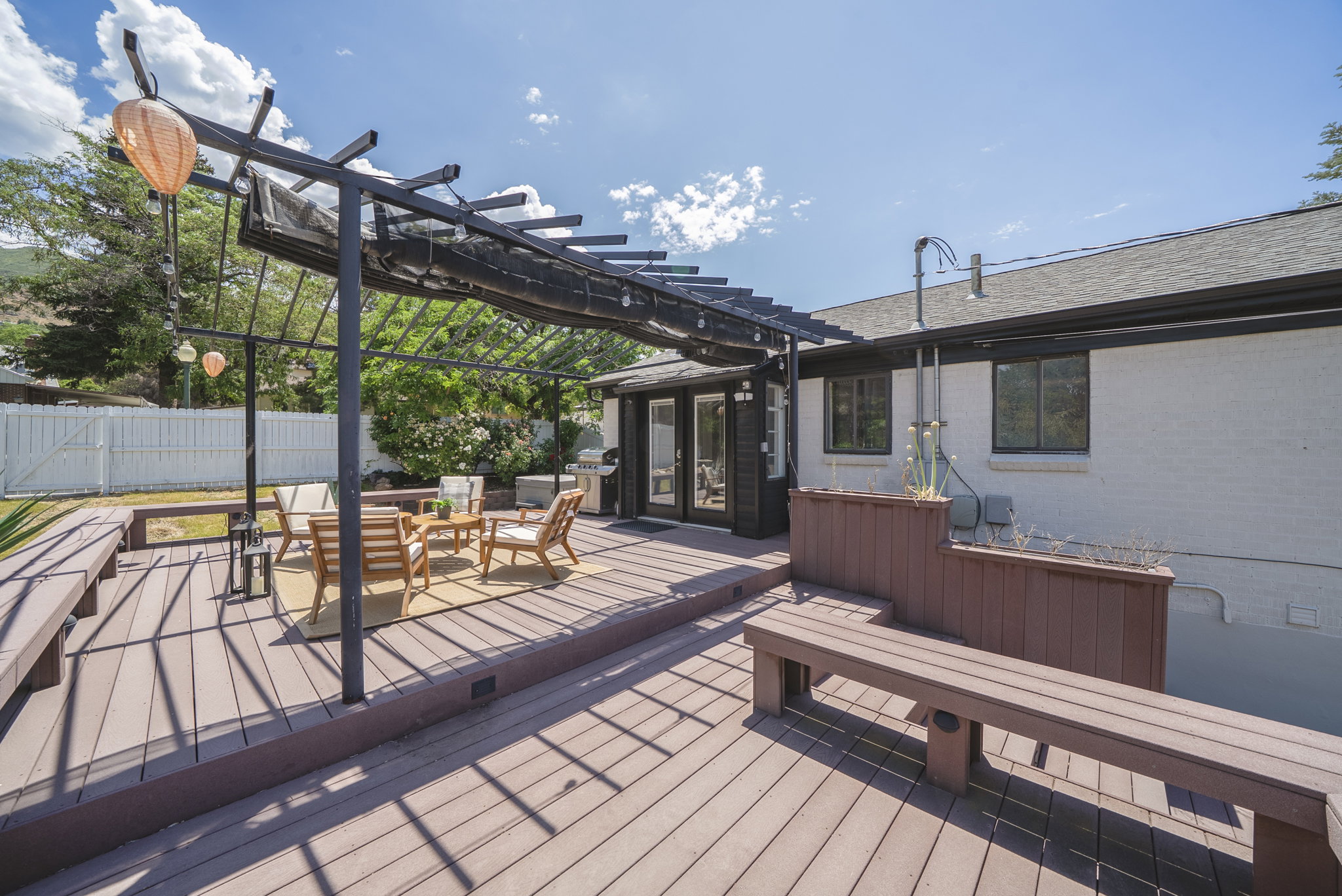 Multi-level deck featuring a pergola with a retractable shade cover, built-in benches, and double glass doors leading into the property