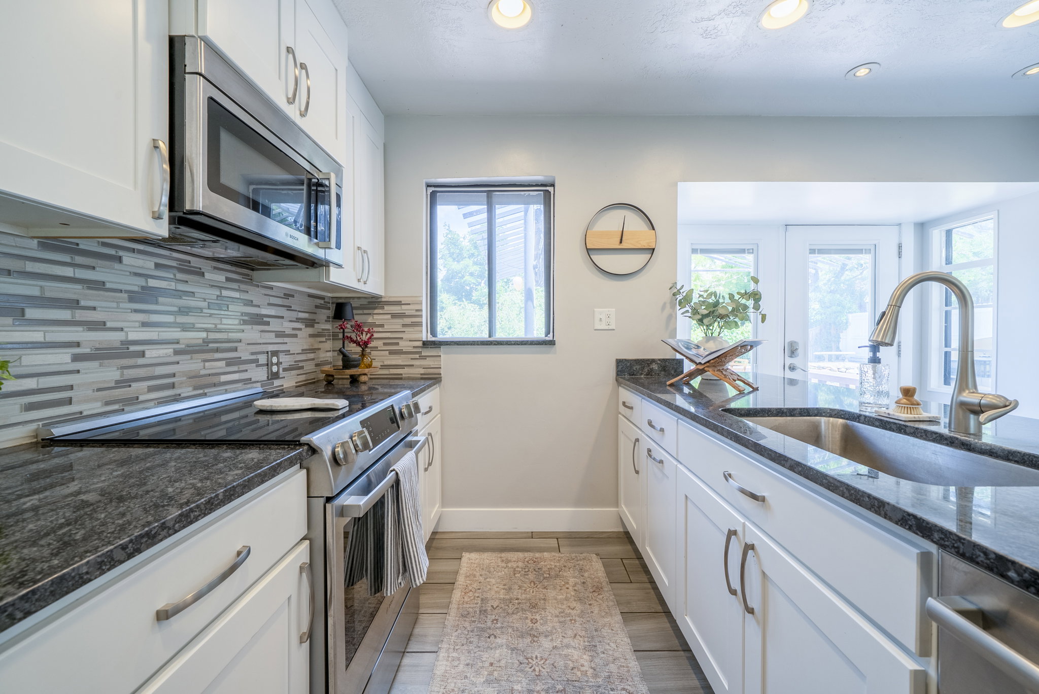 Modern kitchen featuring dark countertops, white cabinetry, stainless steel appliances, a tile backsplash, and recessed lighting