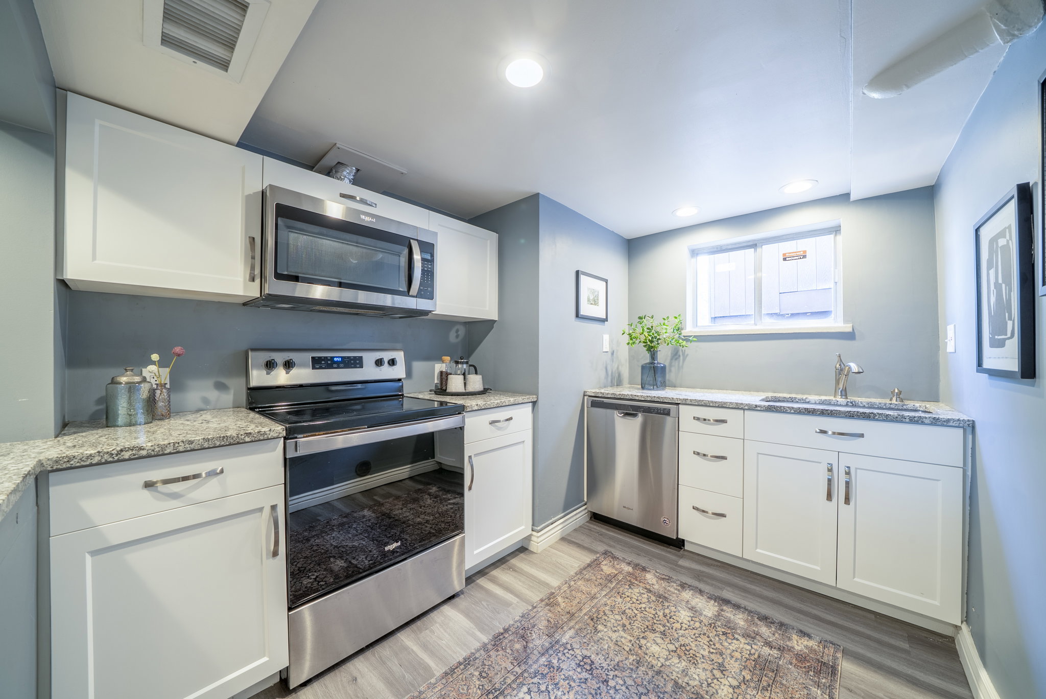 Compact kitchen featuring white shaker-style cabinetry, stainless steel appliances, speckled stone countertops, and wood-finish flooring