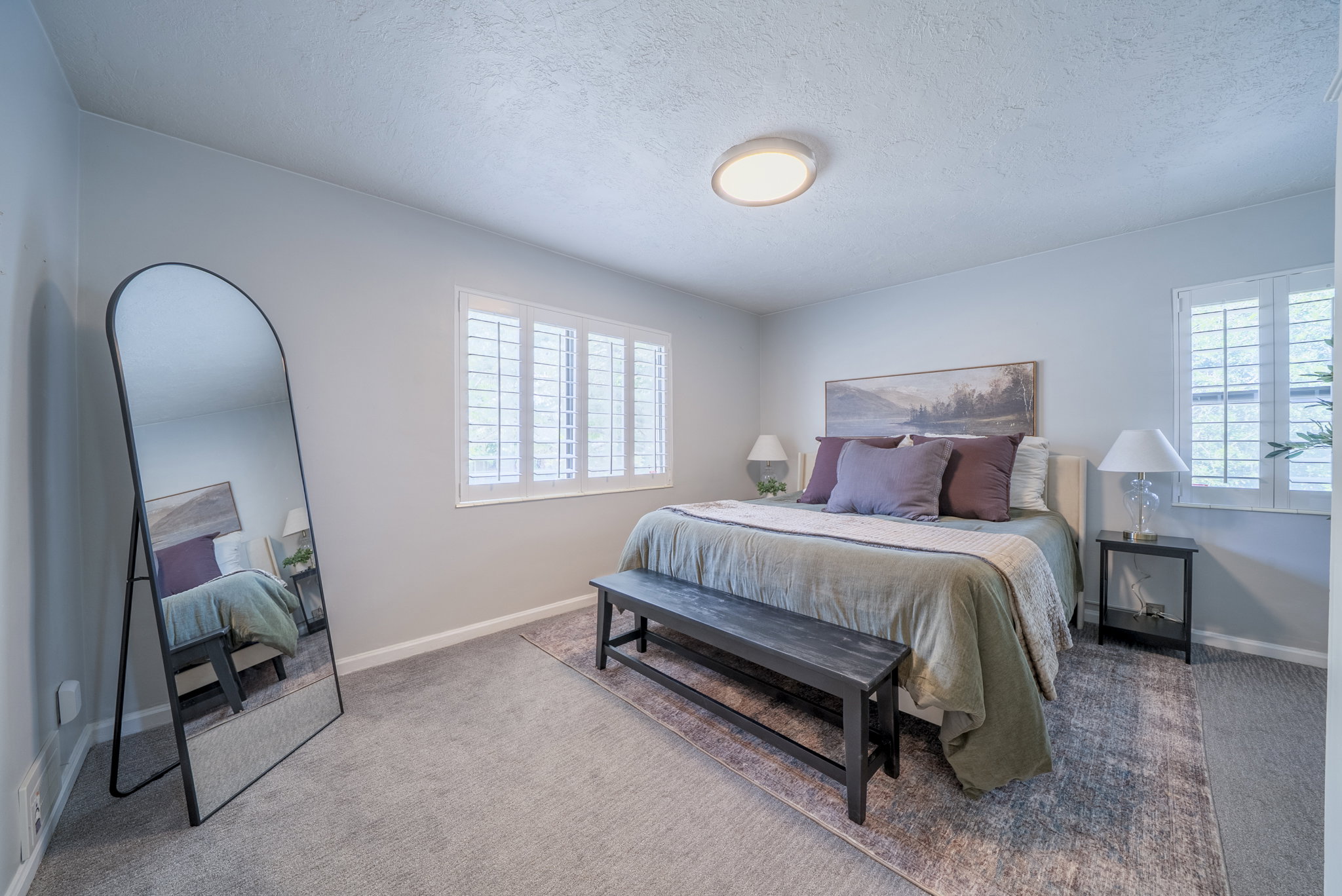 Bedroom featuring wall-to-wall carpeting, dual windows with plantation shutters, a ceiling-mounted light fixture, and light-toned wall finishes