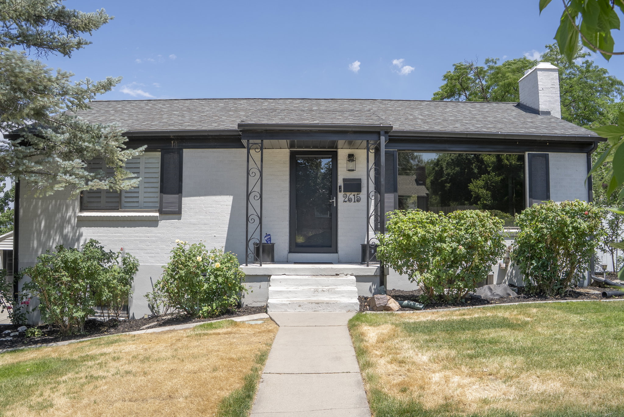White brick exterior with dark trim and a gray asphalt shingle roof