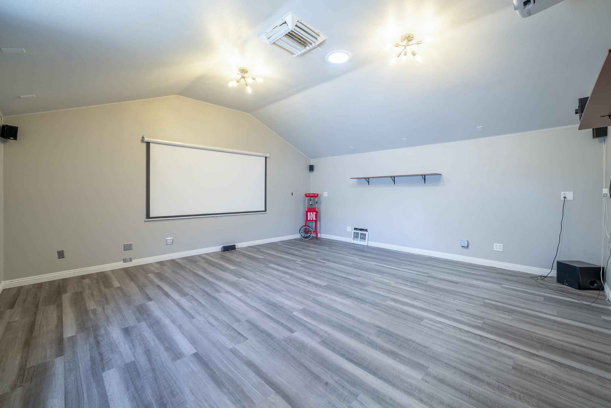 Spacious room featuring vaulted ceilings, wood-finish flooring, a built-in projection screen, and integrated speakers