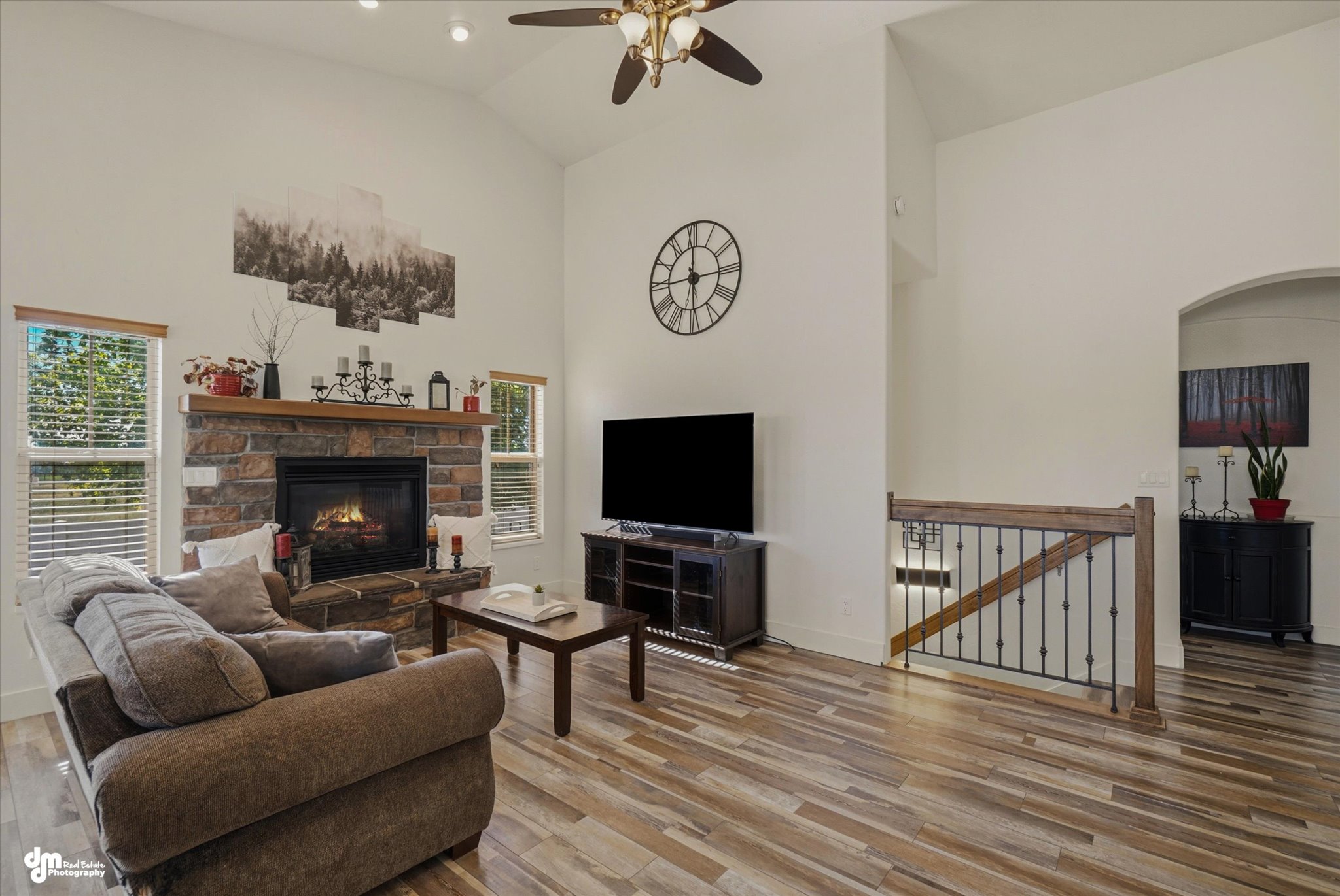 Spacious living area featuring a stone-faced fireplace with wood mantel, vaulted ceilings, and wood-finish flooring