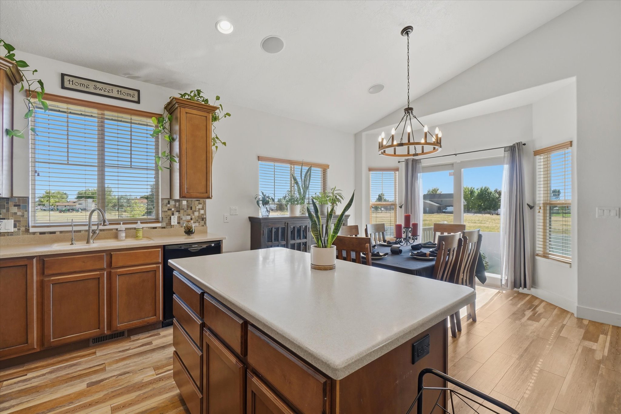 Kitchen and dining area featuring a central island with a light-toned countertop, wood-finish flooring, and vaulted ceilings