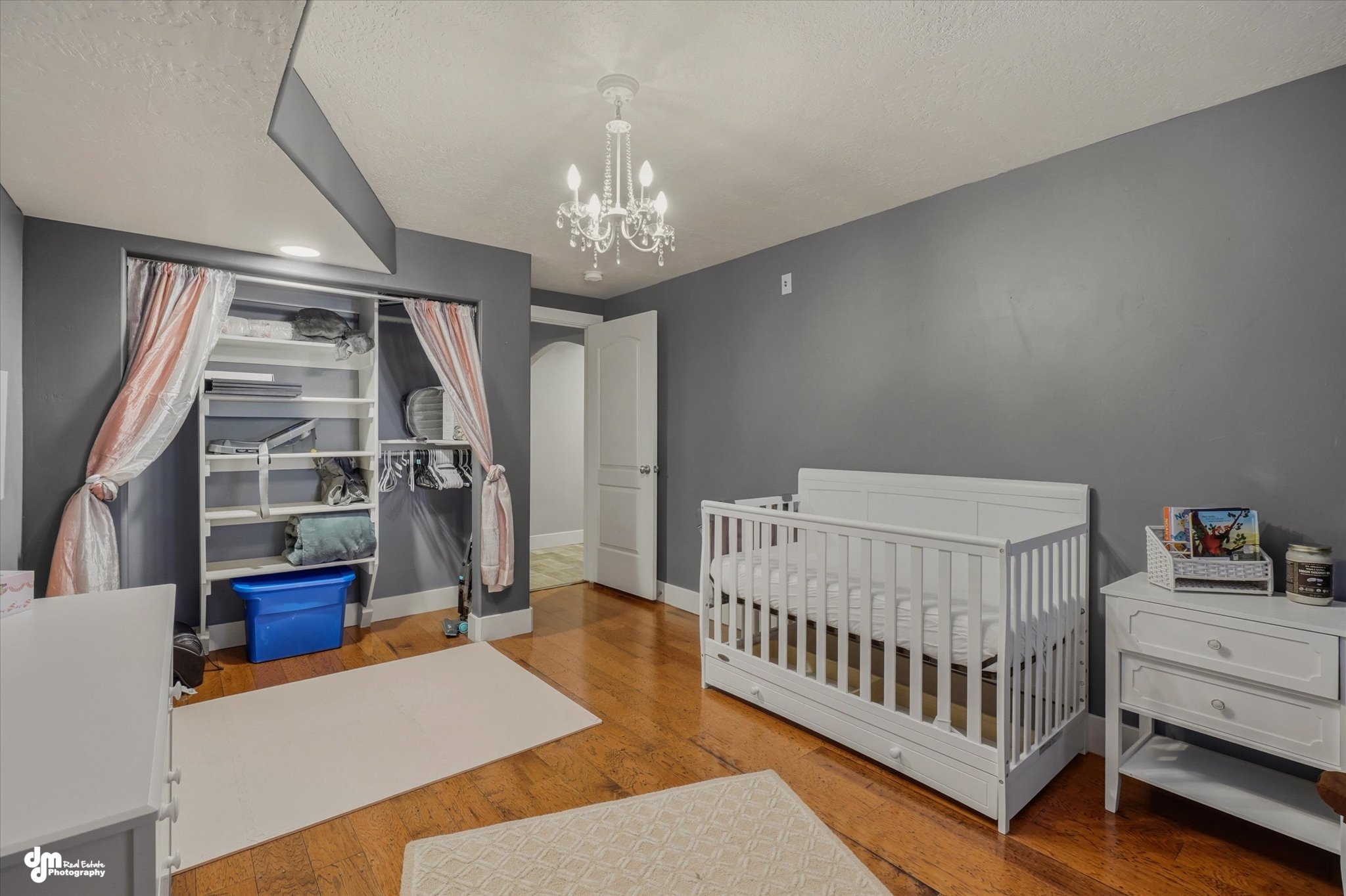 Hardwood flooring throughout featuring a built-in closet organization system, a white crystal chandelier, and a white paneled door