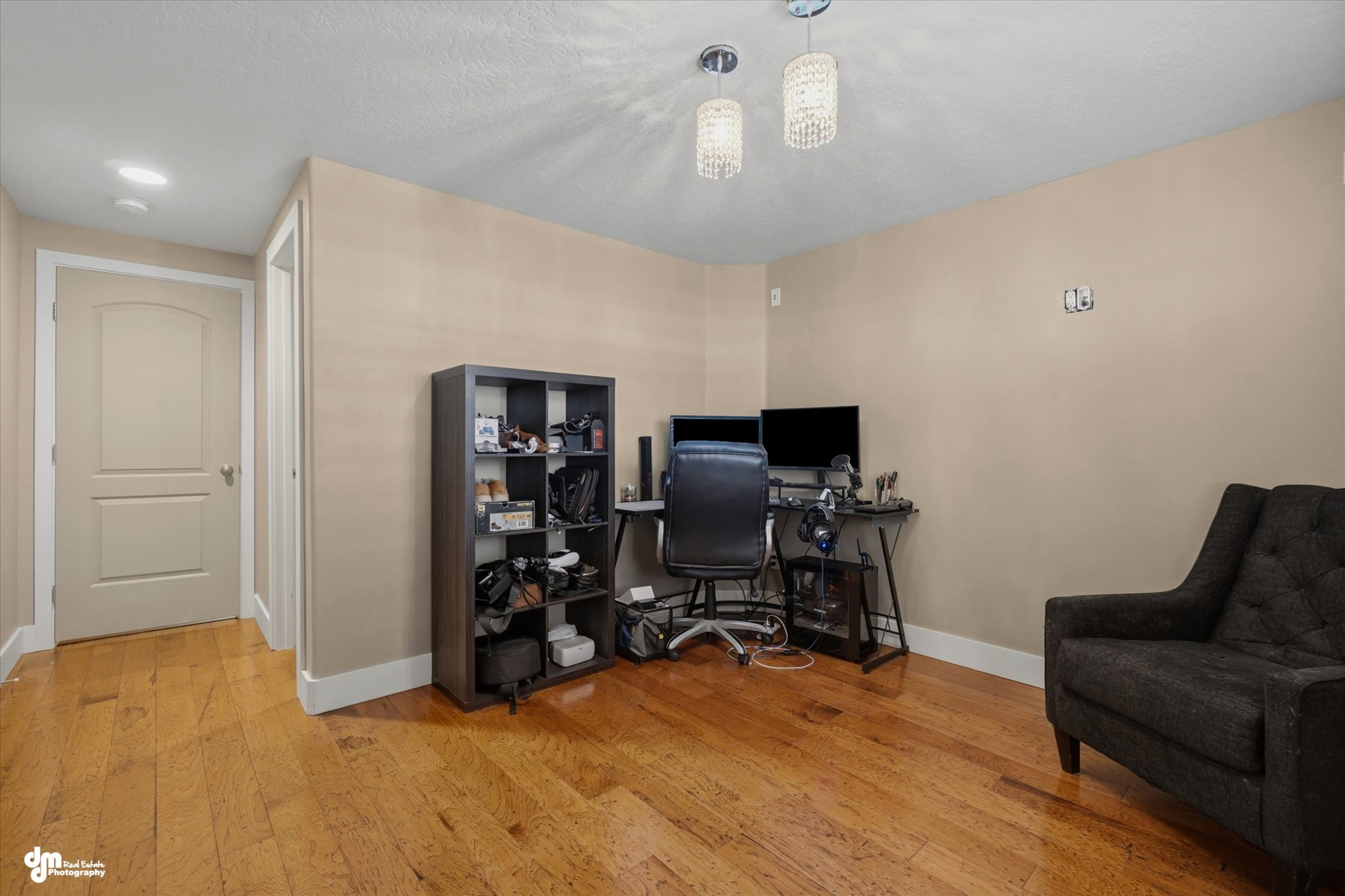 Spacious room featuring wood-finish flooring, neutral-toned walls, white baseboards, and a white ceiling with two pendant light fixtures