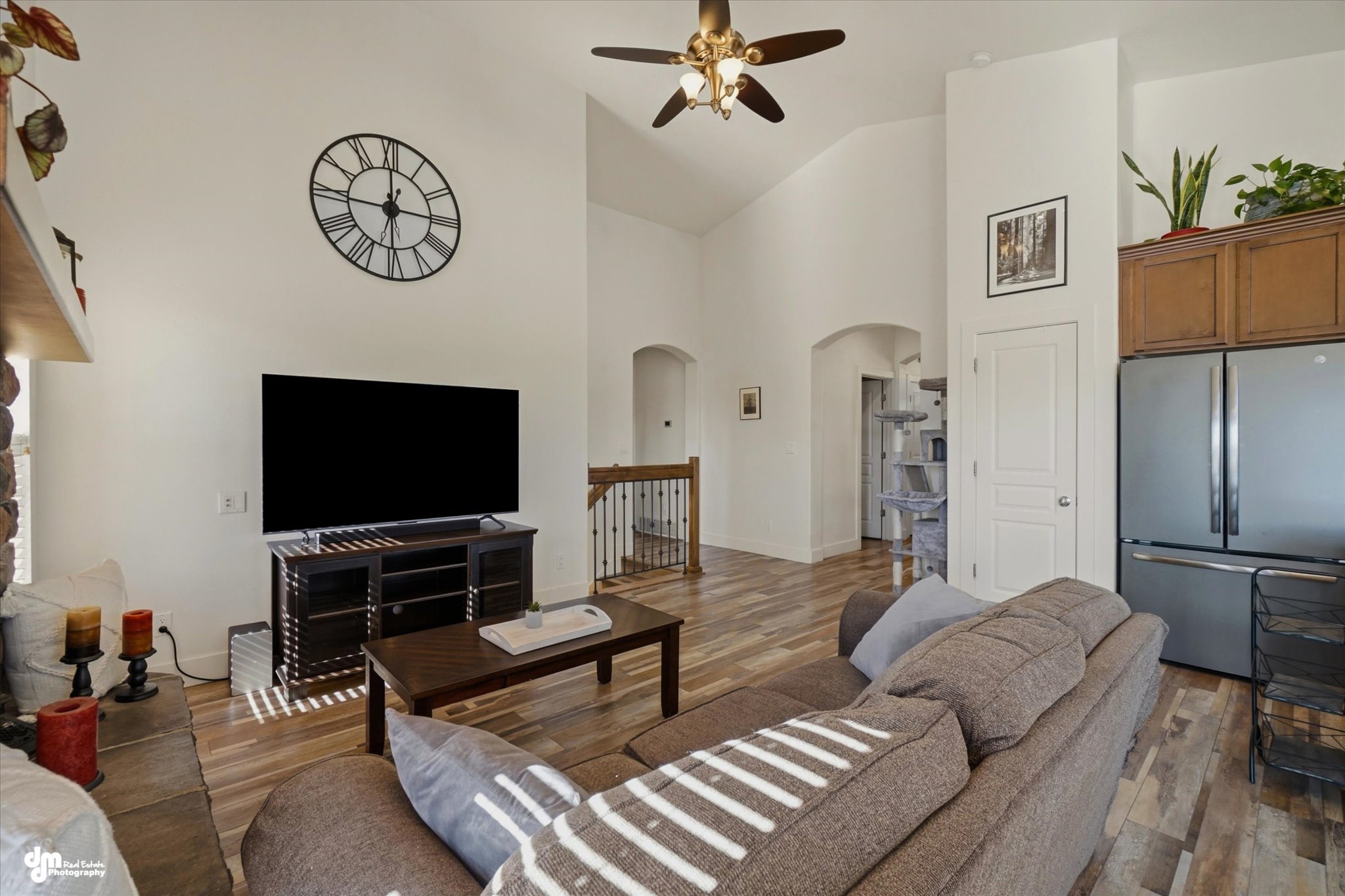 Vaulted ceiling living area featuring wood-finish flooring, a ceiling fan with light fixture, and a built-in stainless steel refrigerator