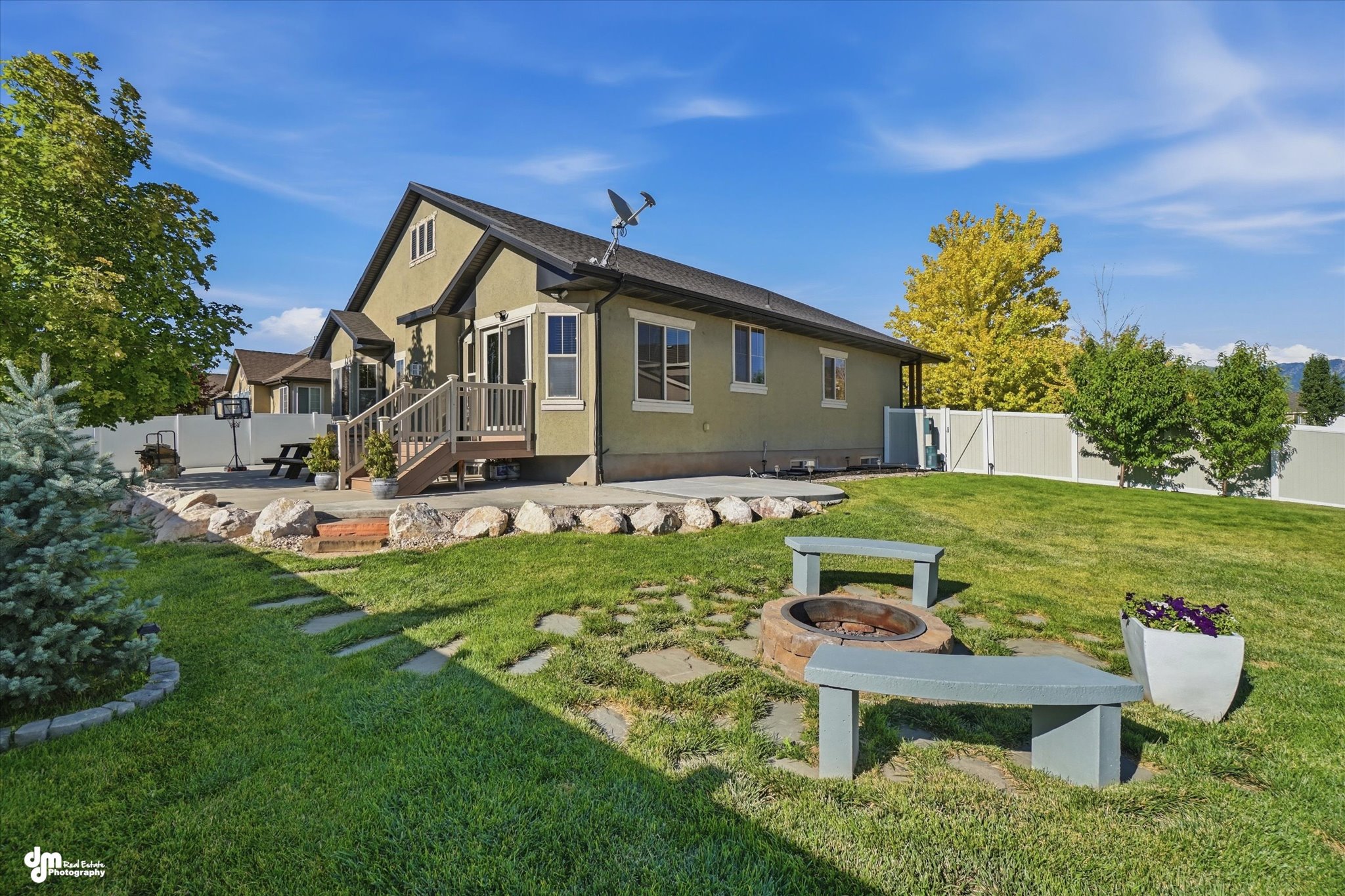 Expansive backyard featuring a manicured lawn, a concrete patio, and a stone fire pit area with built-in benches