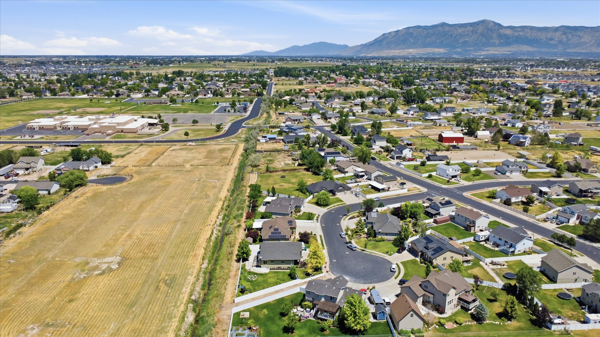 Expansive suburban landscape featuring a mix of residential properties, undeveloped land, and distant mountain ranges