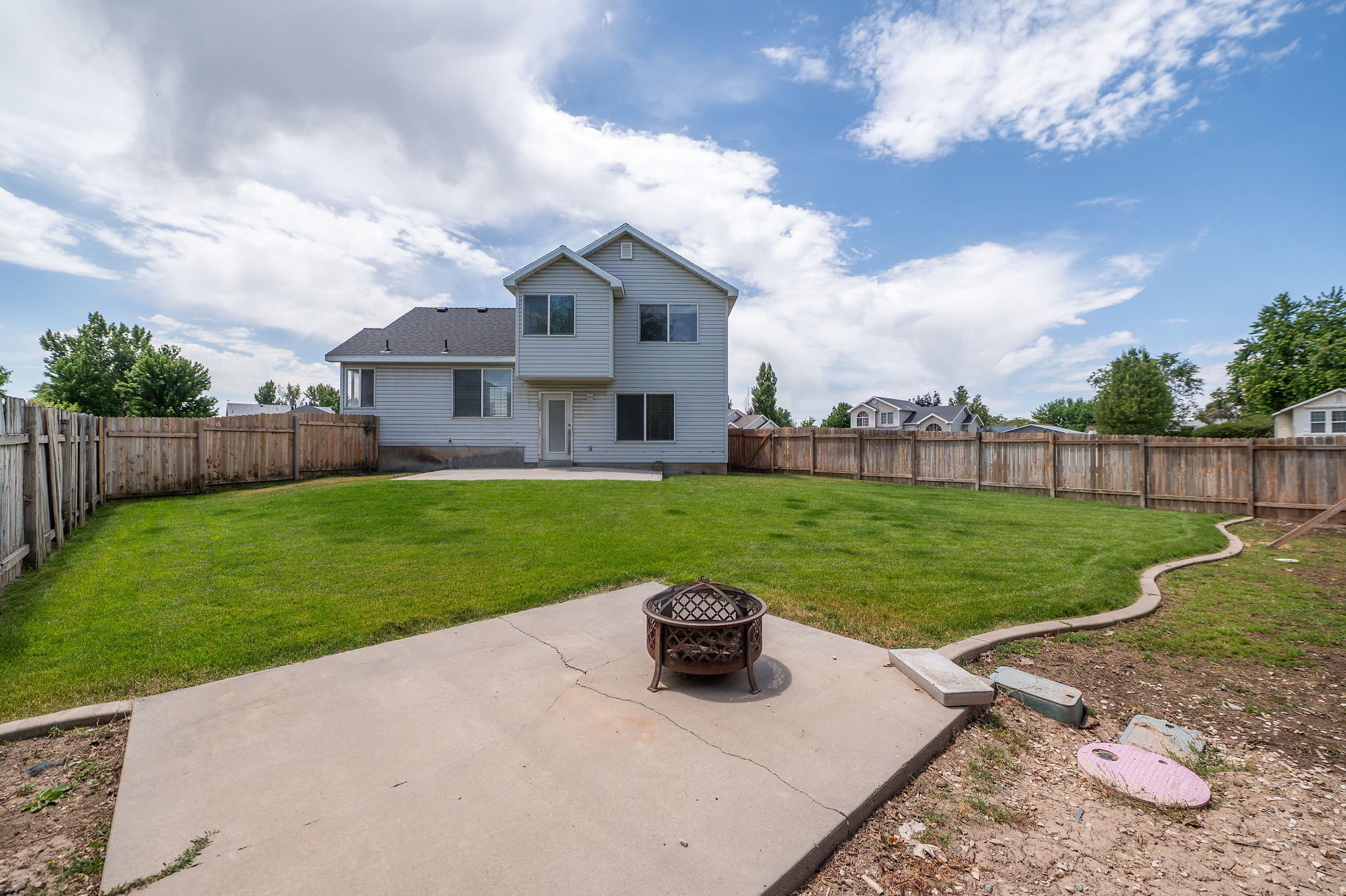 Spacious backyard featuring a manicured lawn, full perimeter wood fencing, and a concrete patio
