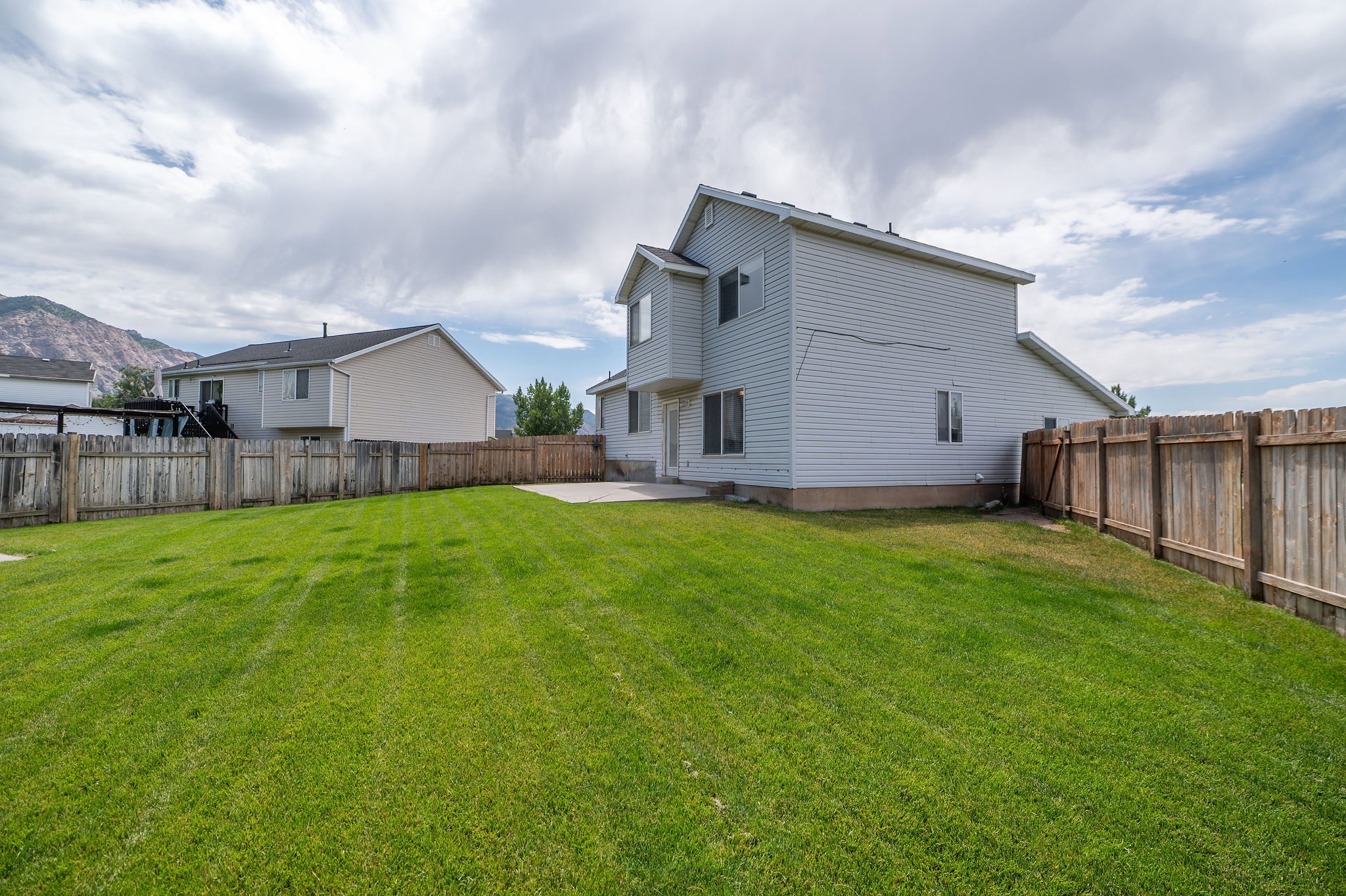 Expansive backyard featuring a manicured lawn, full perimeter wood fencing, and a concrete patio