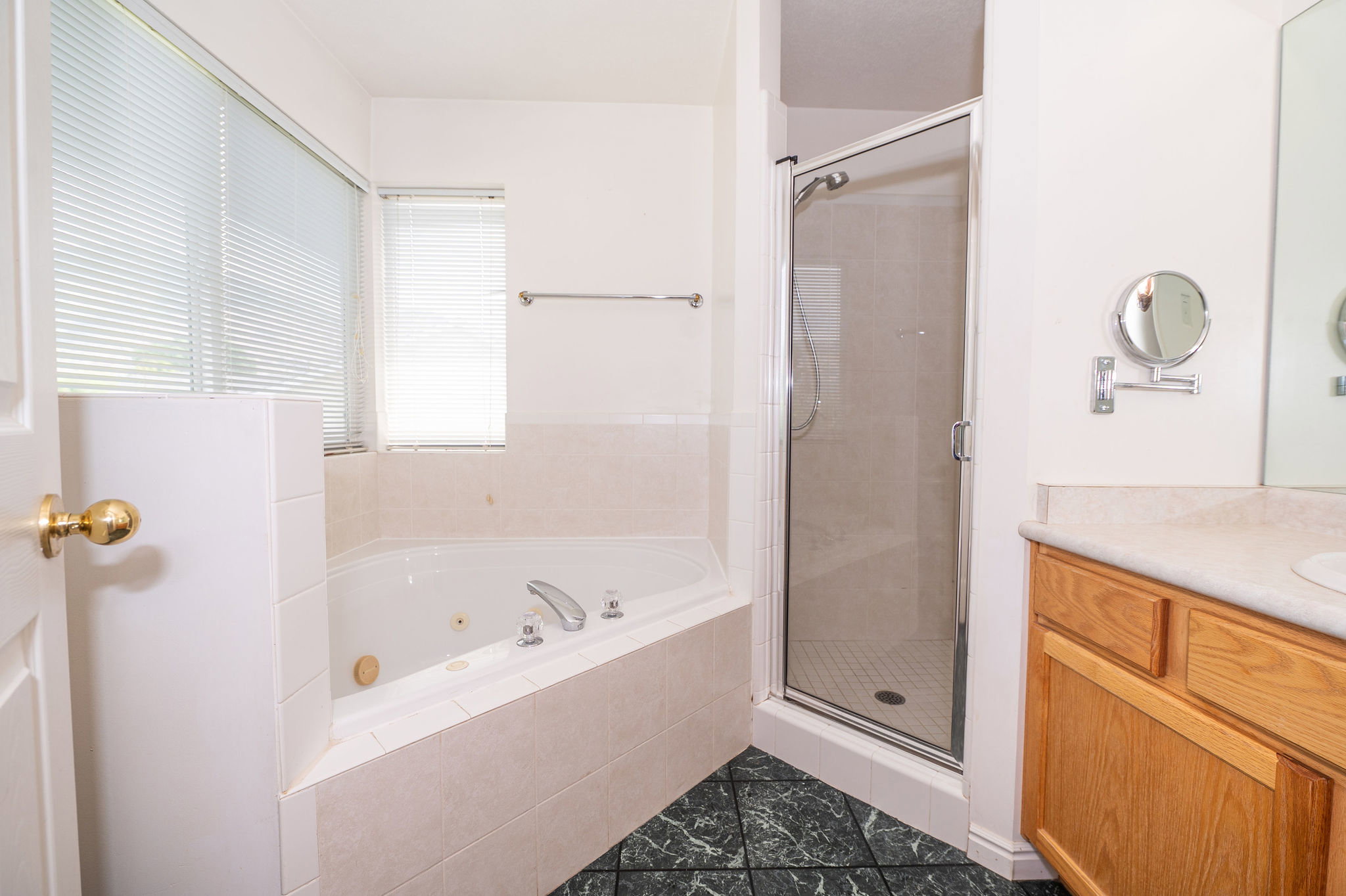 Bathroom with a corner jetted tub, a glass-enclosed shower, a wood-finish vanity with a countertop, and dark patterned floor tiling