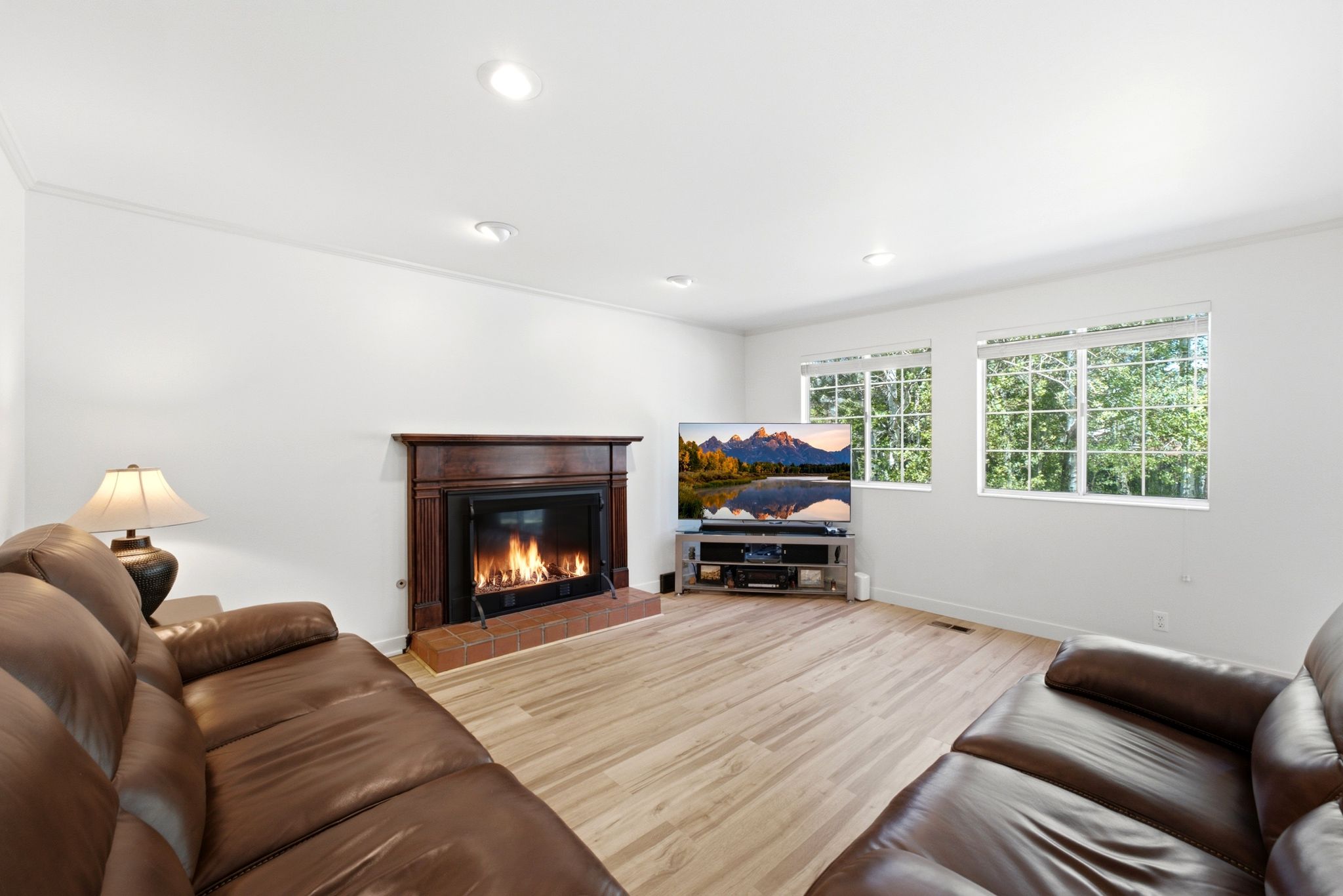 Living area featuring a dark wood-finish mantel over a fireplace with a brick hearth, light wood-finish flooring, and two windows