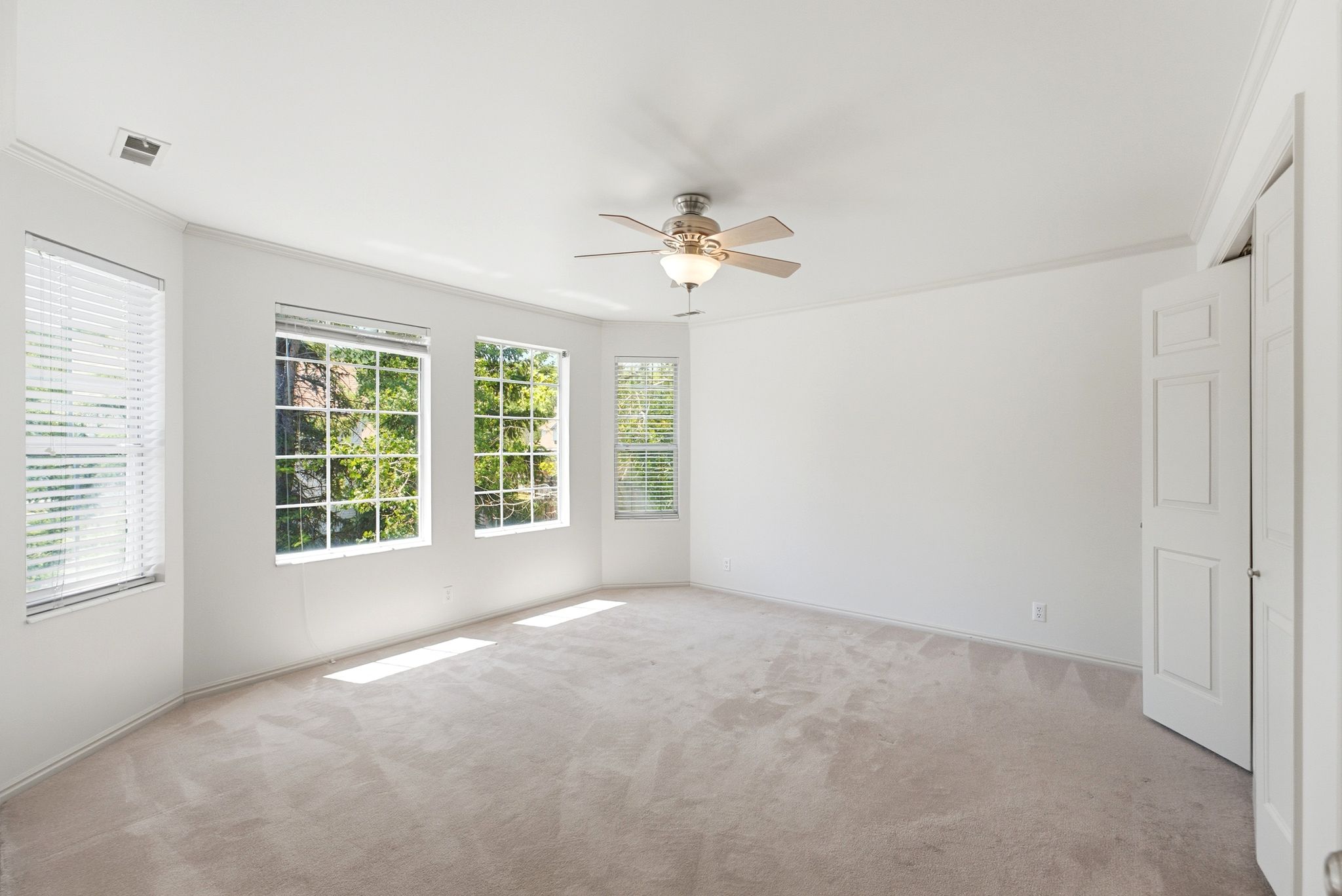 Spacious room featuring multiple windows with blinds, light-colored carpeting, a ceiling fan with integrated lighting, and crown molding