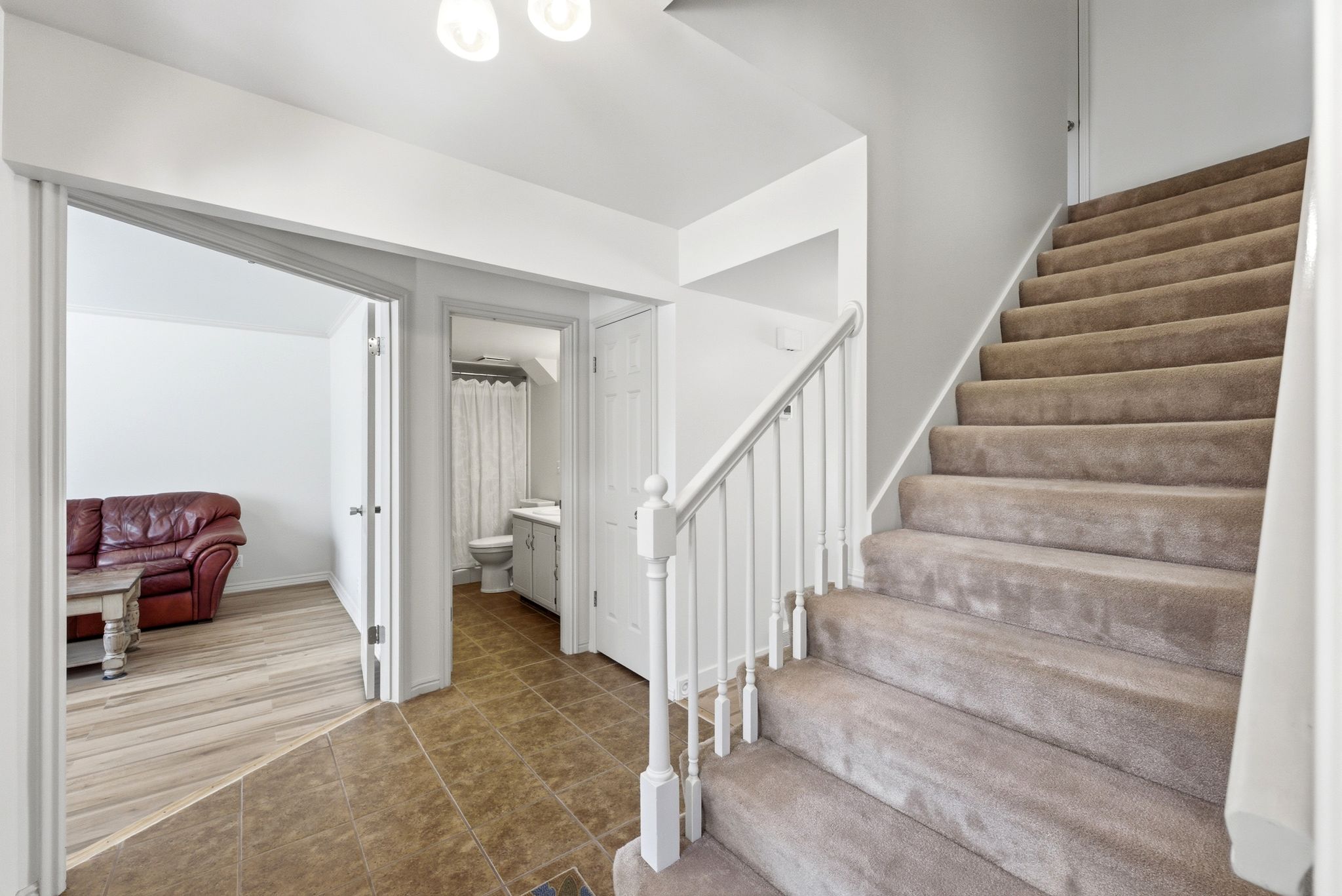 Inviting entryway featuring a carpeted staircase with white railings, tile flooring, and access to a room with wood-finish flooring