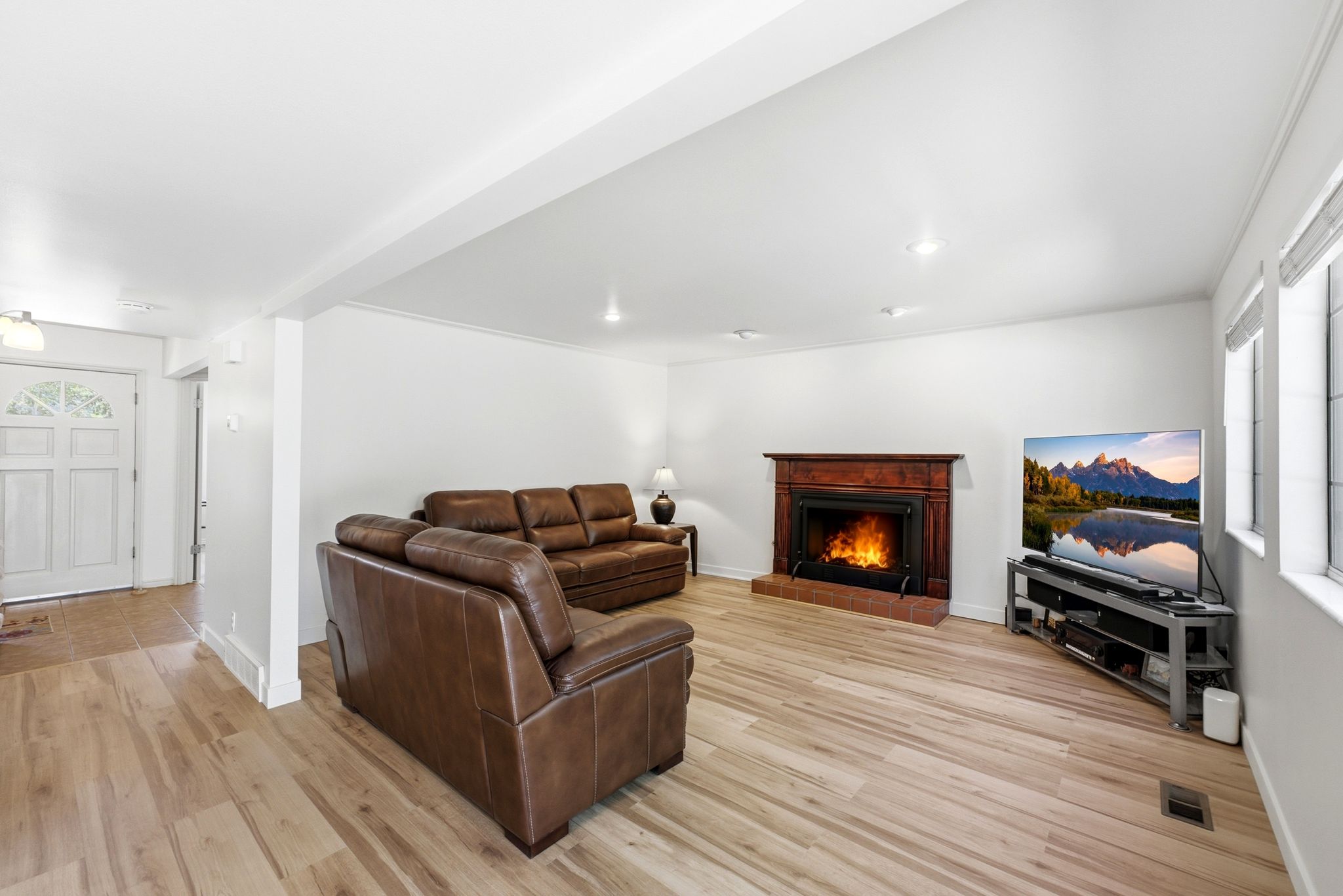 Living area featuring wood-finish flooring, a wood-surround fireplace with a brick hearth, recessed lighting, and multiple windows
