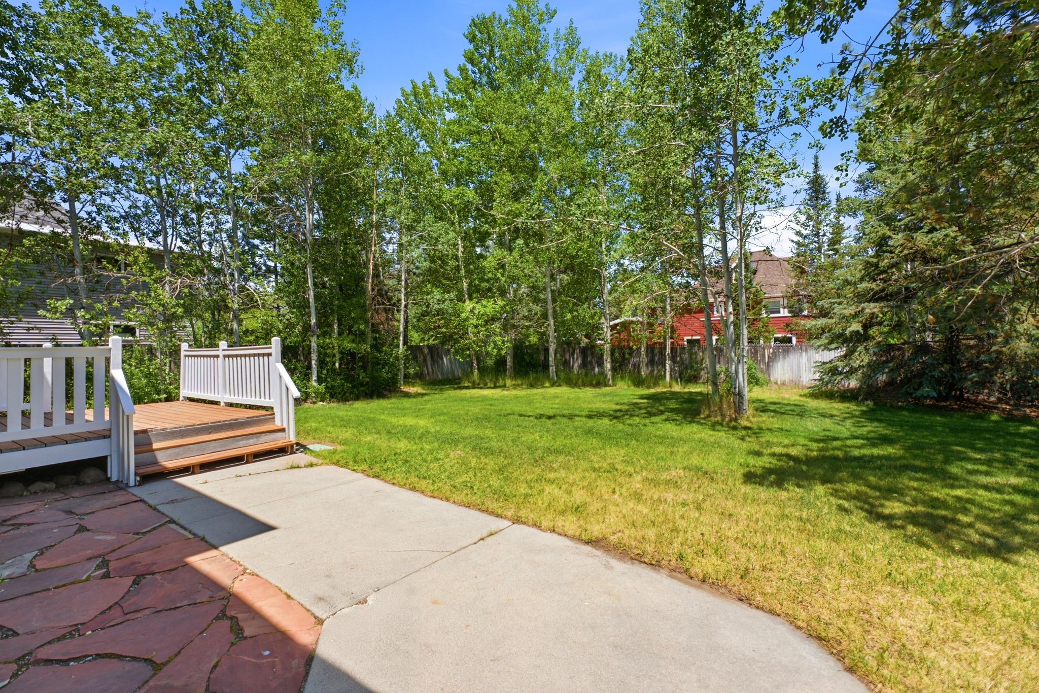 Expansive backyard featuring a lush lawn, mature trees, and a flagstone patio