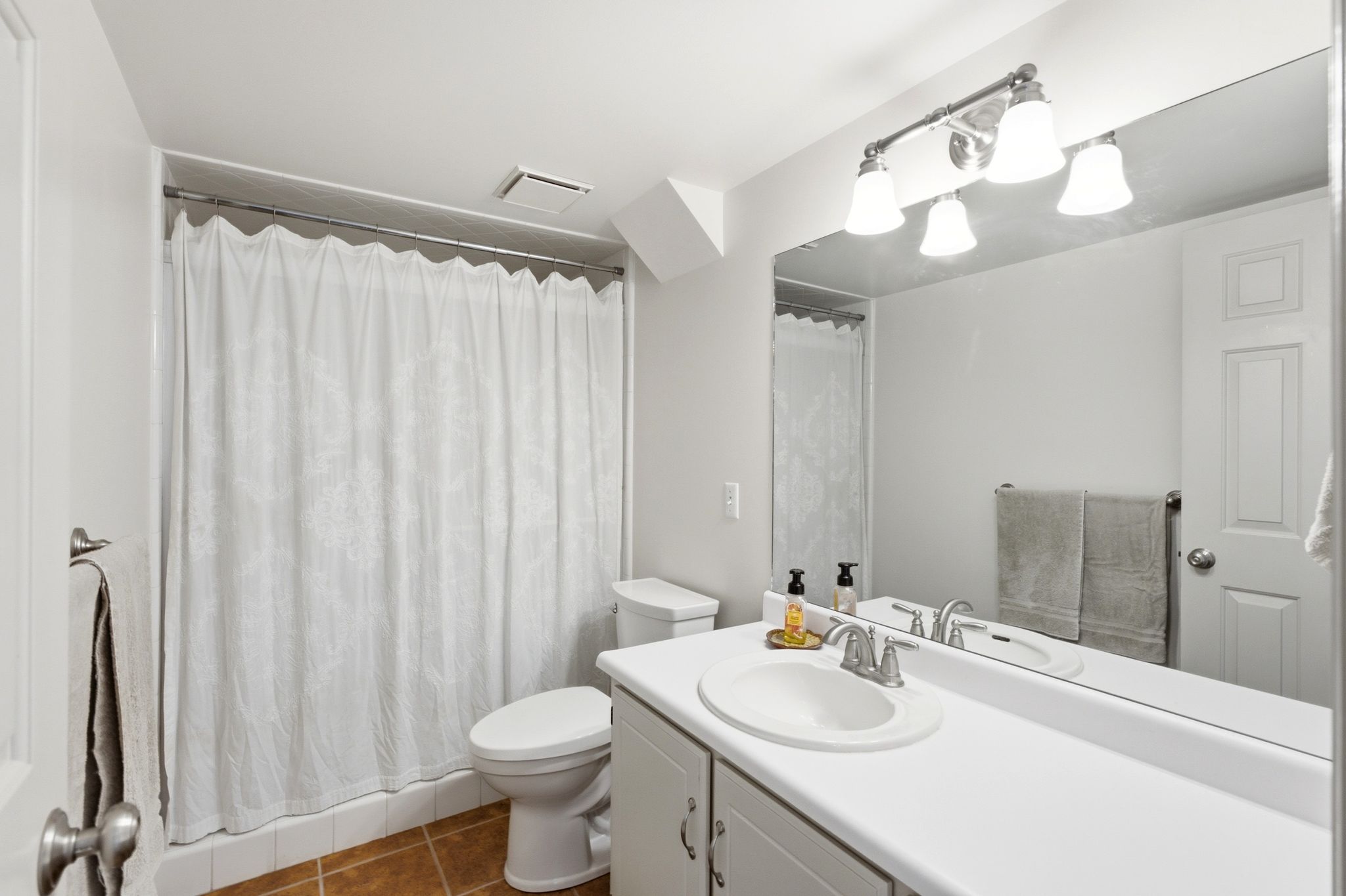Bathroom featuring a full vanity with an integrated sink, broad wall mirror, and a four-light fixture