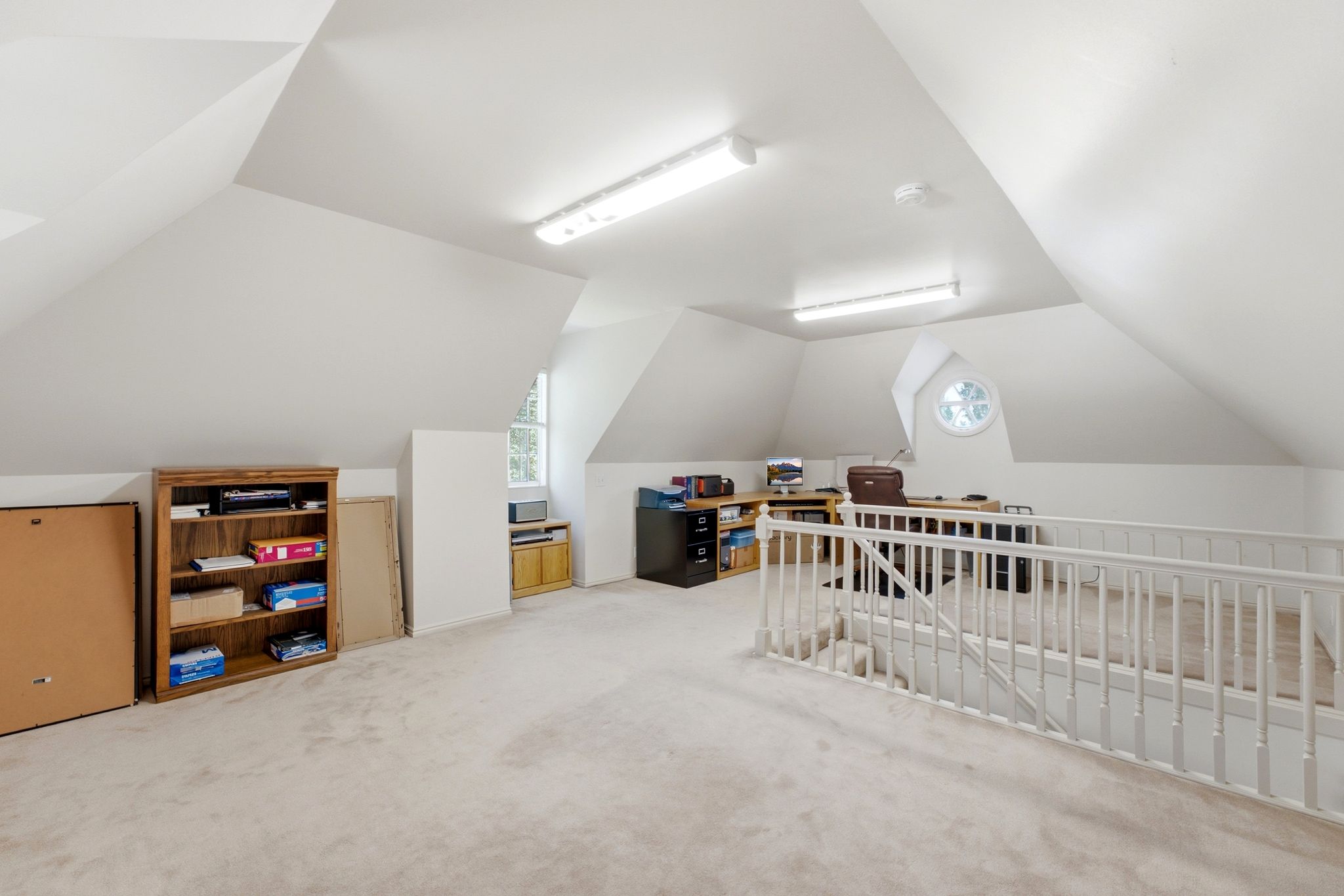 Spacious loft area featuring sloped ceilings, white carpeting, and a round architectural window