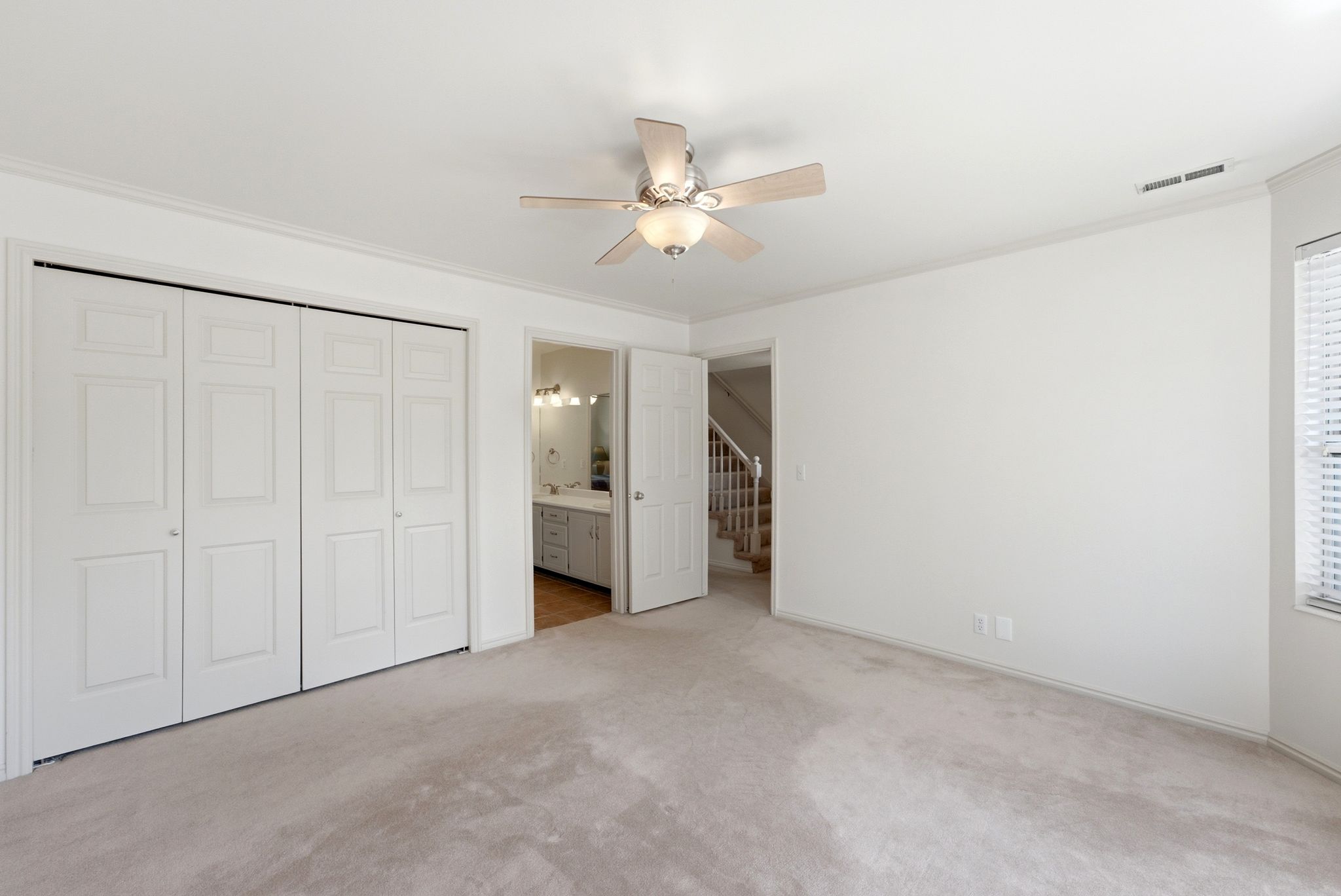 Spacious interior room featuring light-toned carpeting, a ceiling fan, and white bi-fold closet doors