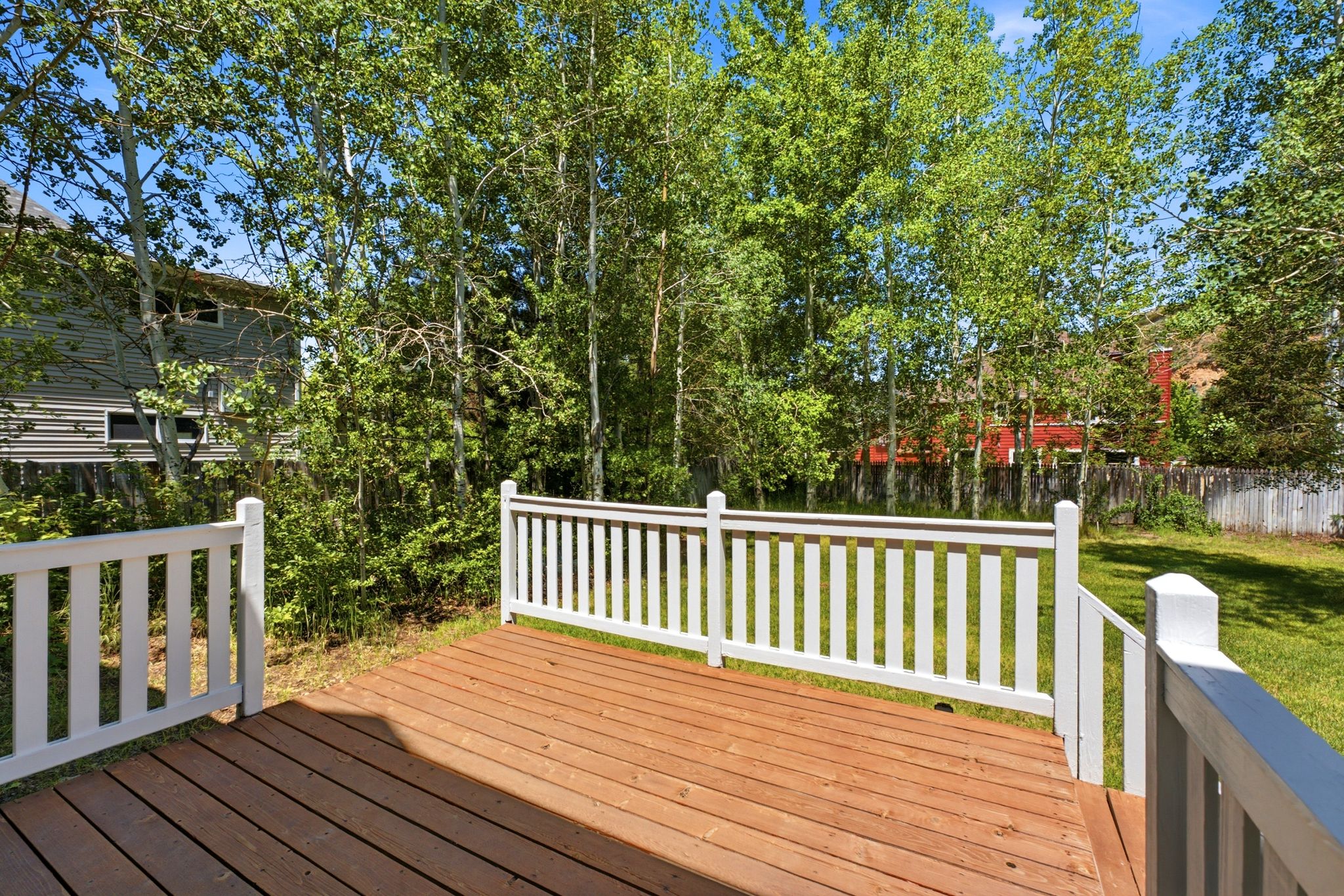Spacious wood-finish deck with white railings overlooking a green lawn and mature trees