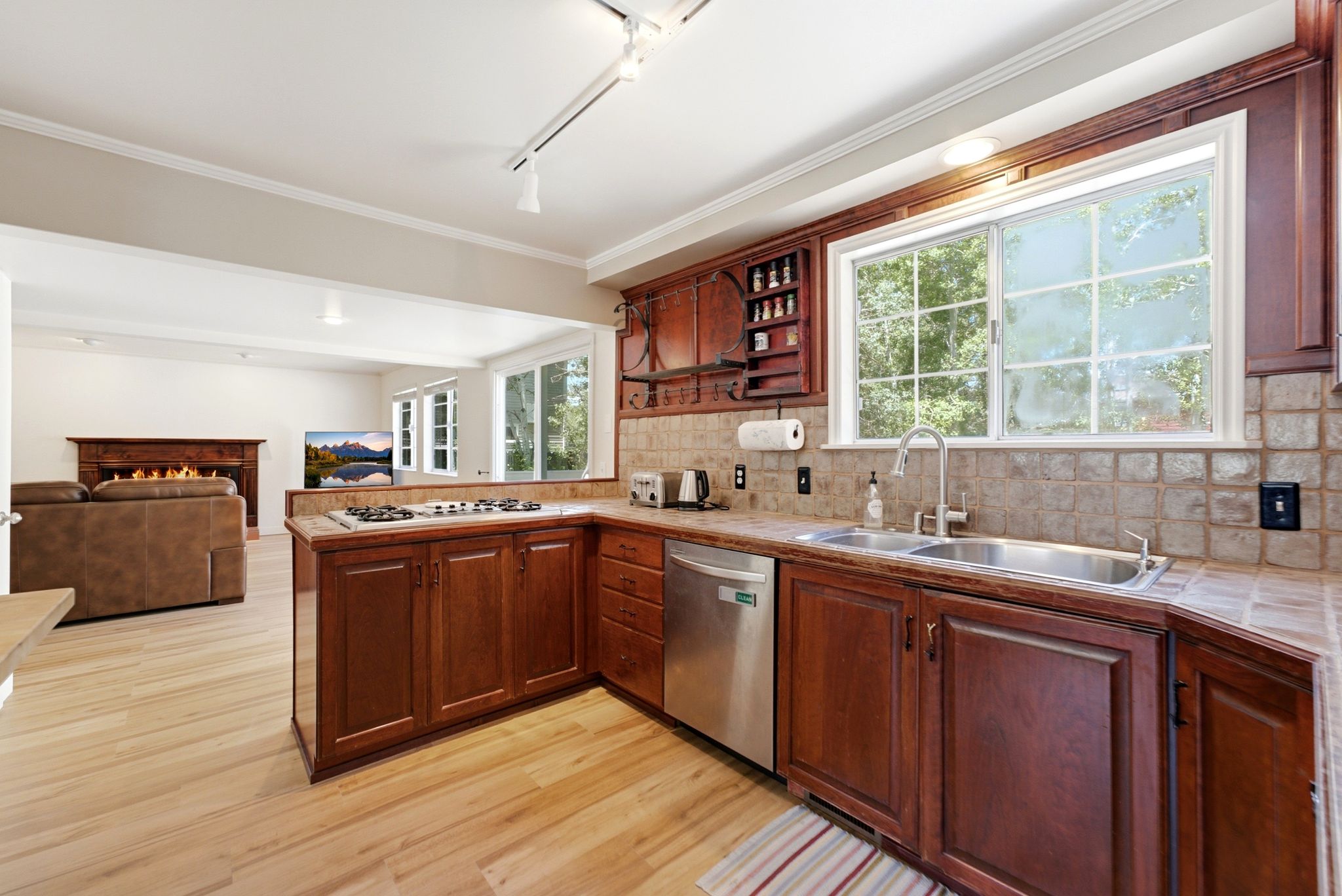 Kitchen featuring wood-finish cabinetry, tile countertops, a double basin sink with a gooseneck faucet, a stainless steel dishwasher, and a gas cooktop