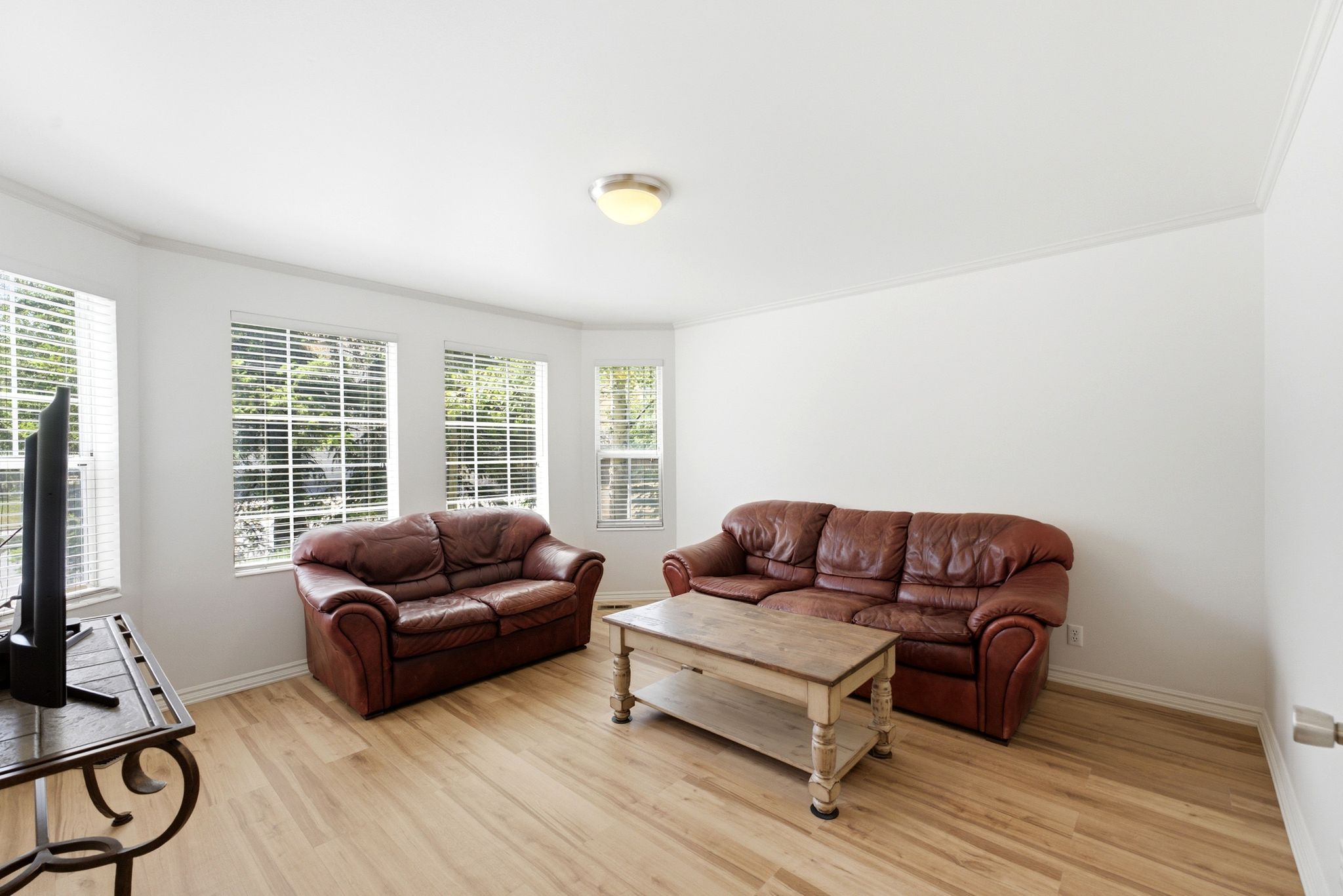 Bay window configuration featuring multiple windows with blinds, wood-finish flooring, white walls, and crown molding