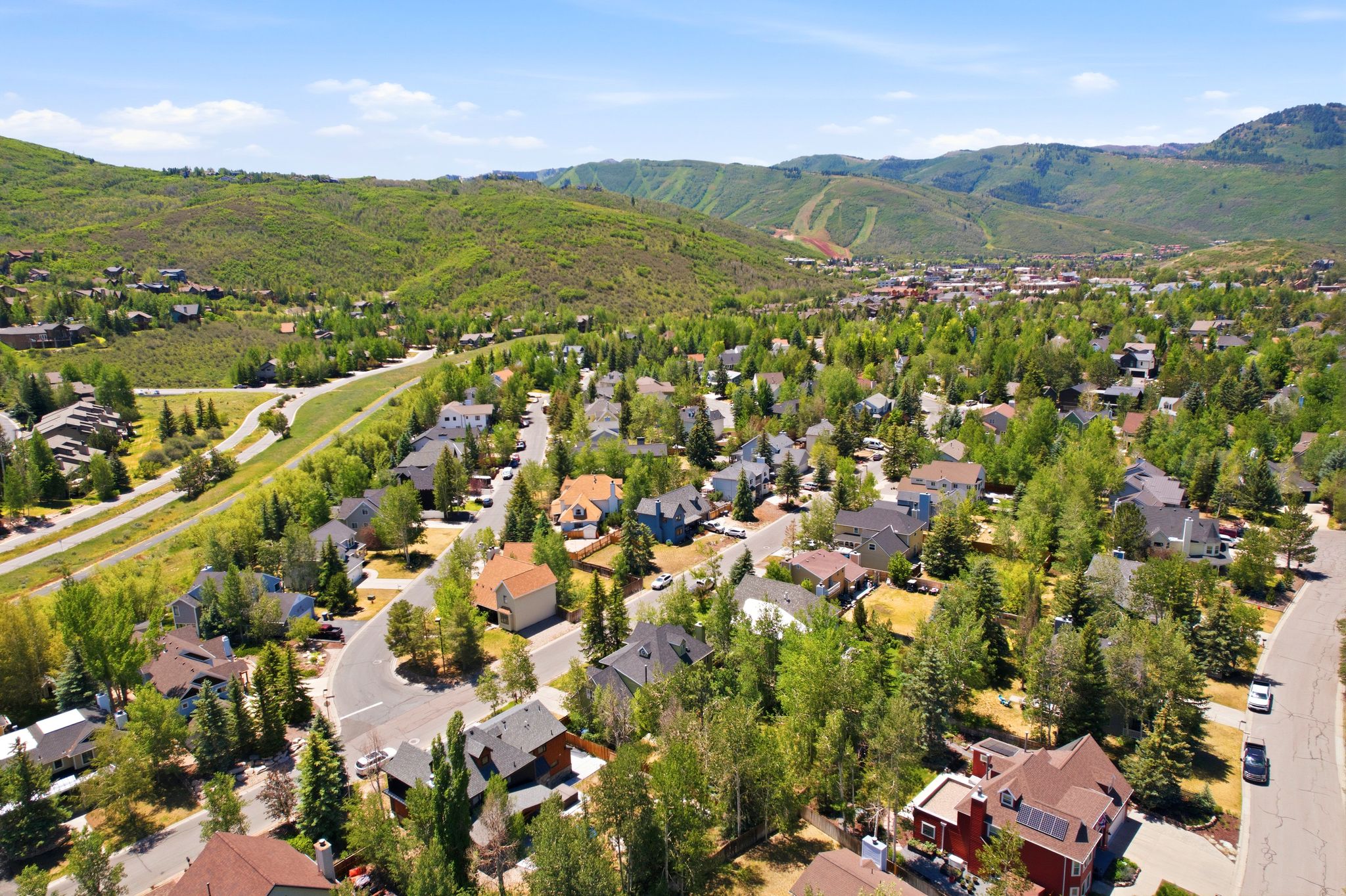 Expansive residential area featuring numerous properties surrounded by mature trees, winding roads, and verdant hillsides