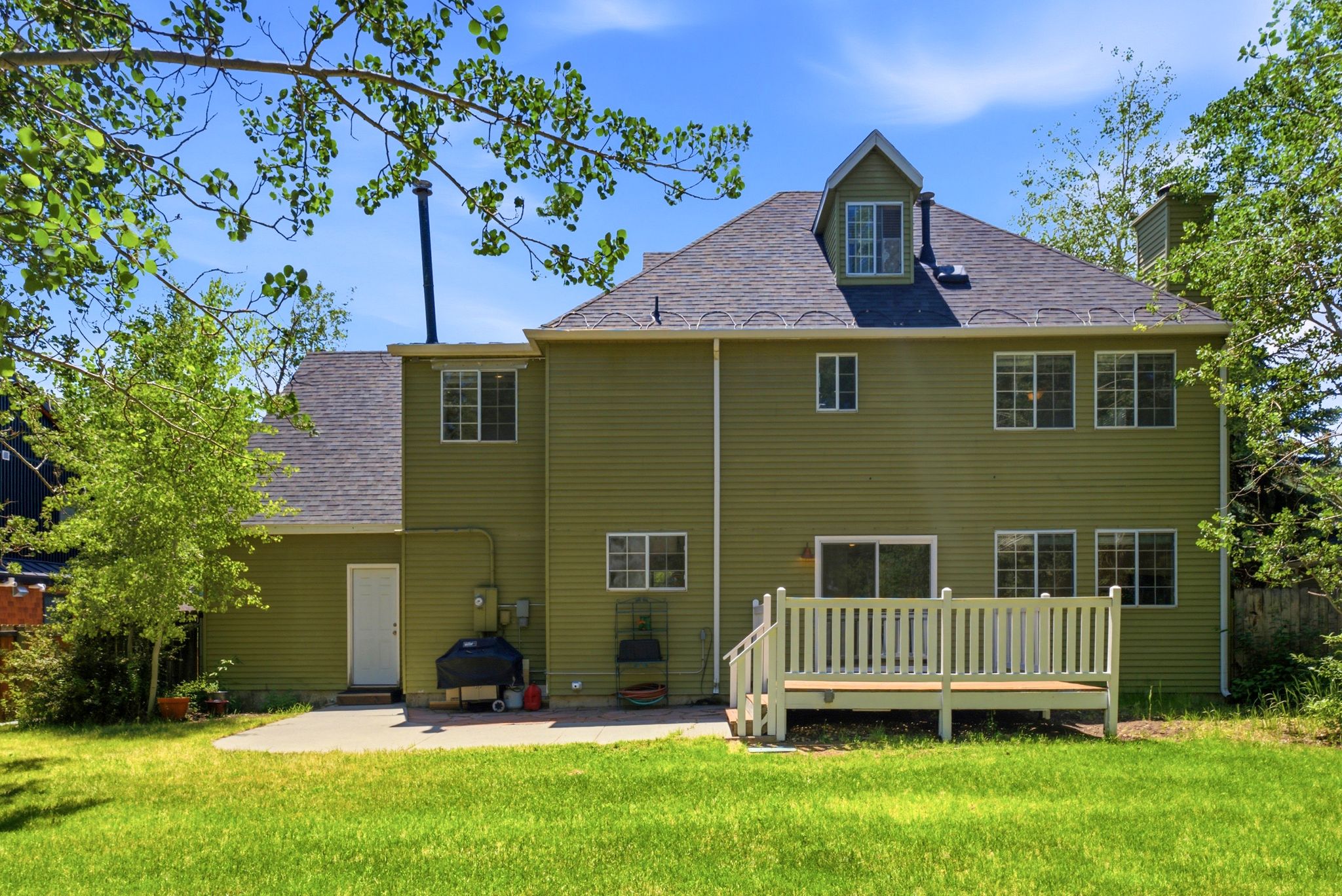 Expansive green exterior with a multi-level roofline, a dormer window, and multiple windows across the rear facade