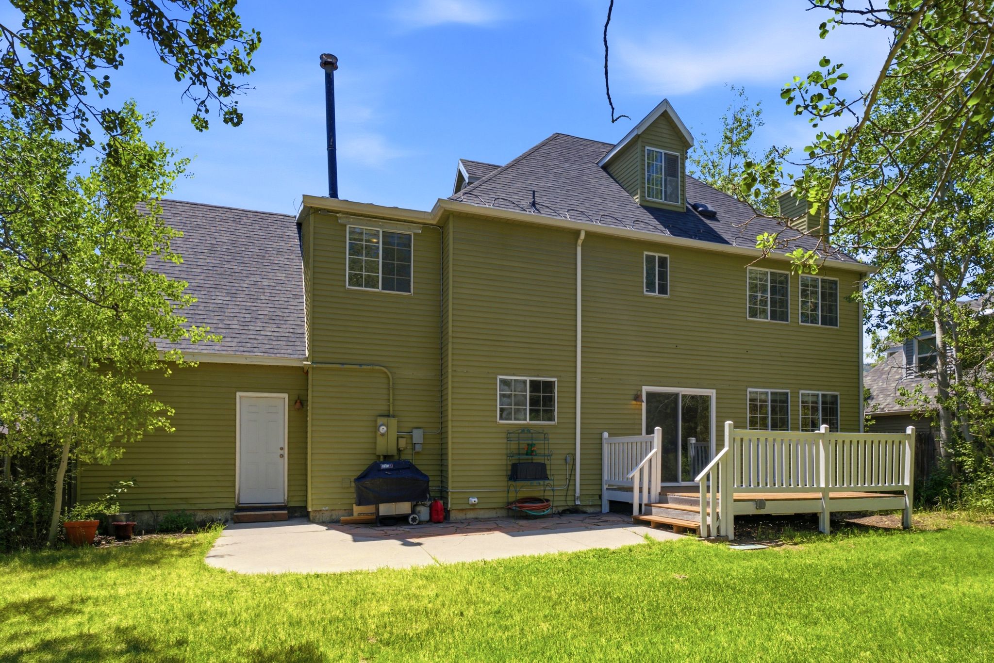 Rear exterior featuring siding, a multi-level roofline, numerous windows, and a sliding glass door leading to a wooden deck with railing