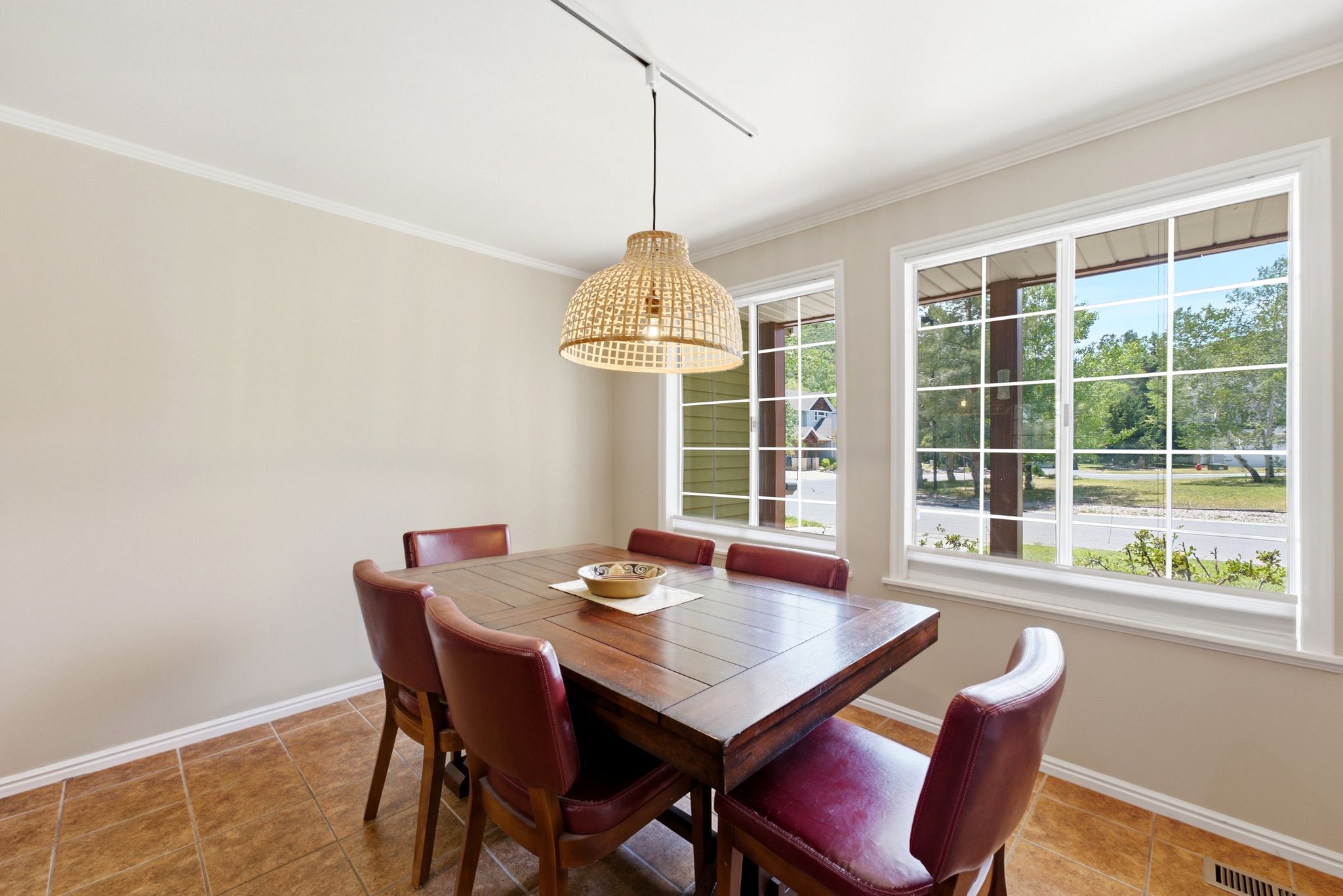 Warm dining area featuring two large windows, tile flooring, and a decorative woven pendant light fixture
