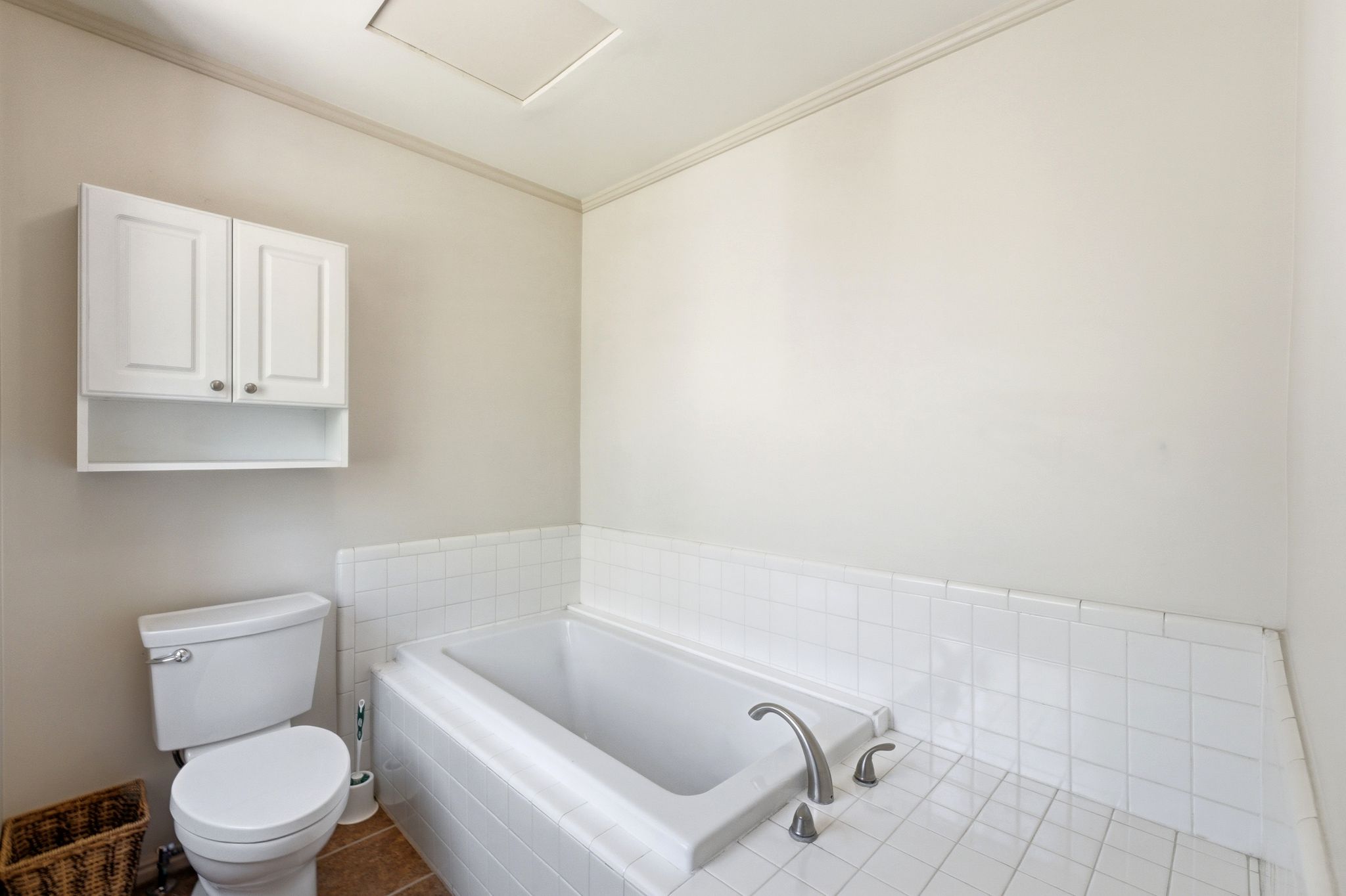 Bathroom featuring a built-in tub with tile surround, white wall cabinets, and a toilet