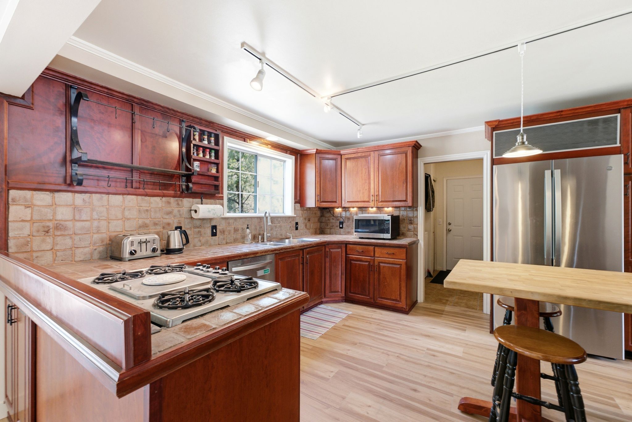Kitchen featuring wood-finish cabinetry, tile countertops, a built-in cooktop, and light wood-finish flooring