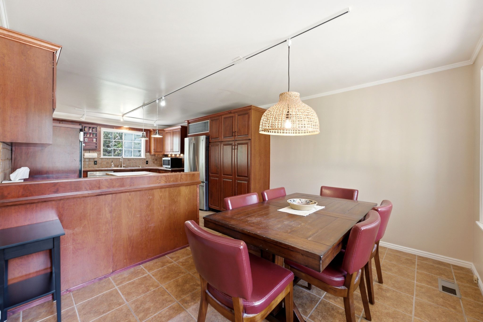 Dining area with a woven pendant light, wood-finish flooring, and crown molding, opening to a kitchen with stainless steel appliances, wood cabinetry, and a window over the sink