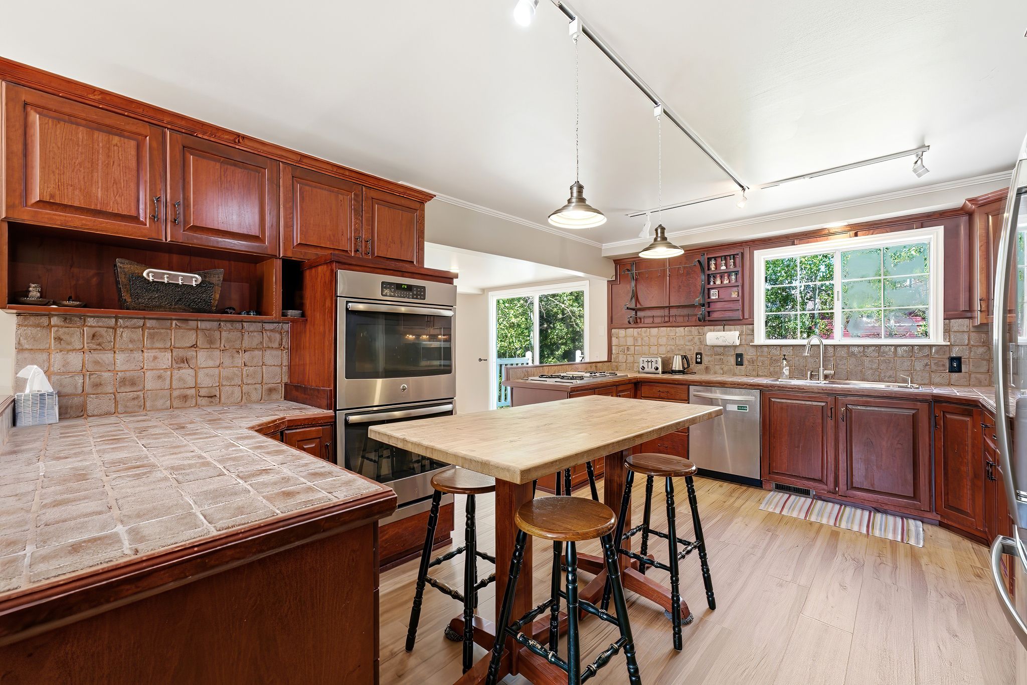 Kitchen featuring wood cabinetry, stainless steel double oven, tiled countertops, and wood-finish flooring