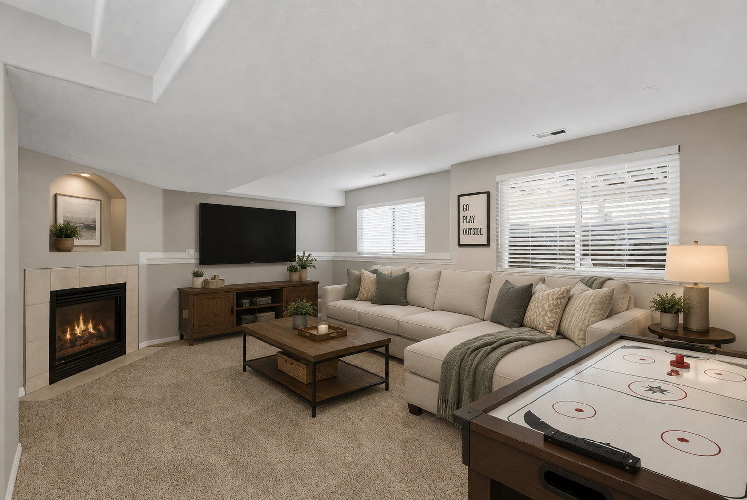 Carpeted recreation room featuring a corner fireplace with tile surround, built-in niche, and multiple windows with blinds. Staged virtually.