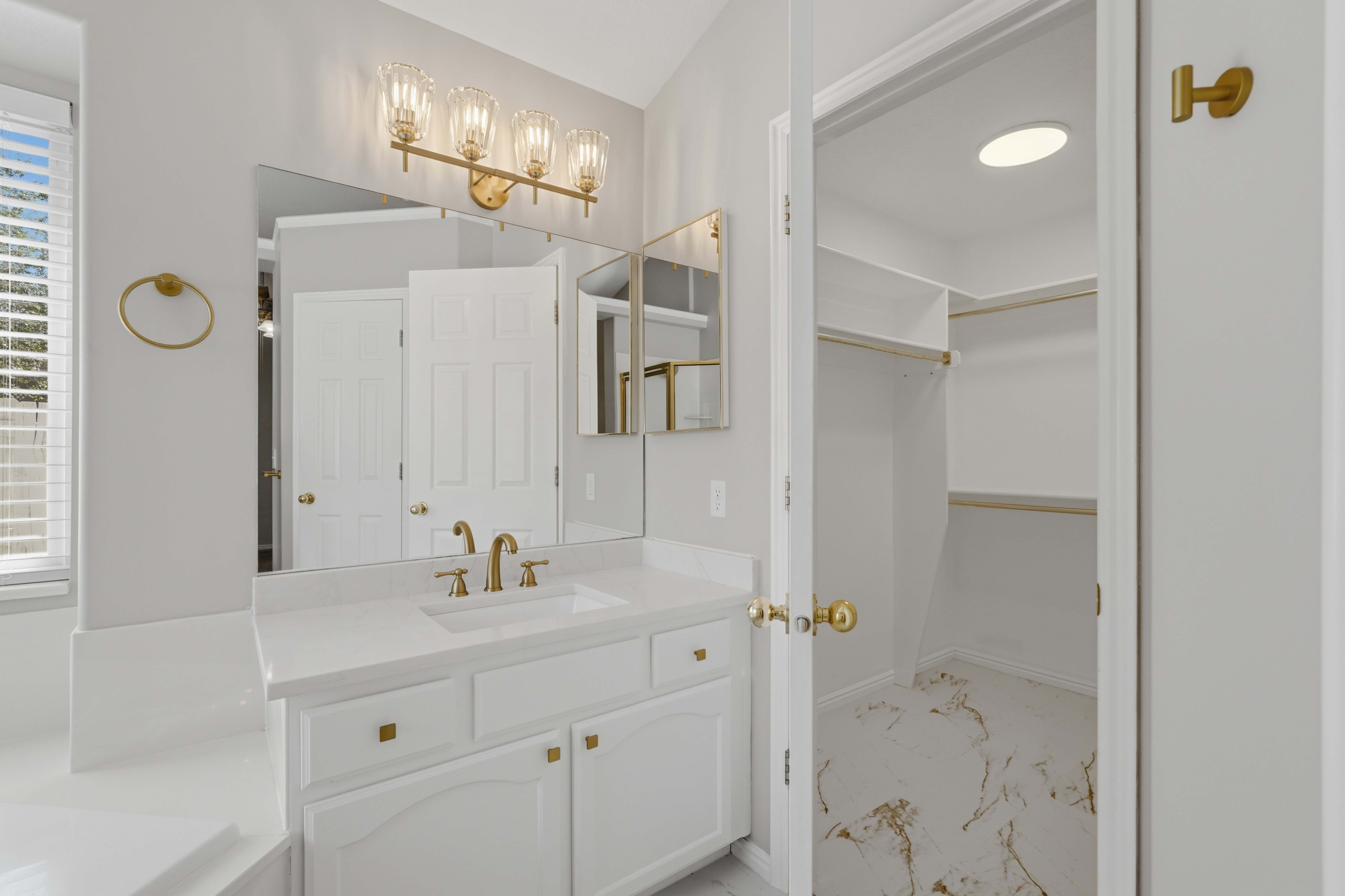 Bathroom vanity with a white countertop, undermount sink, and brass-finish faucet