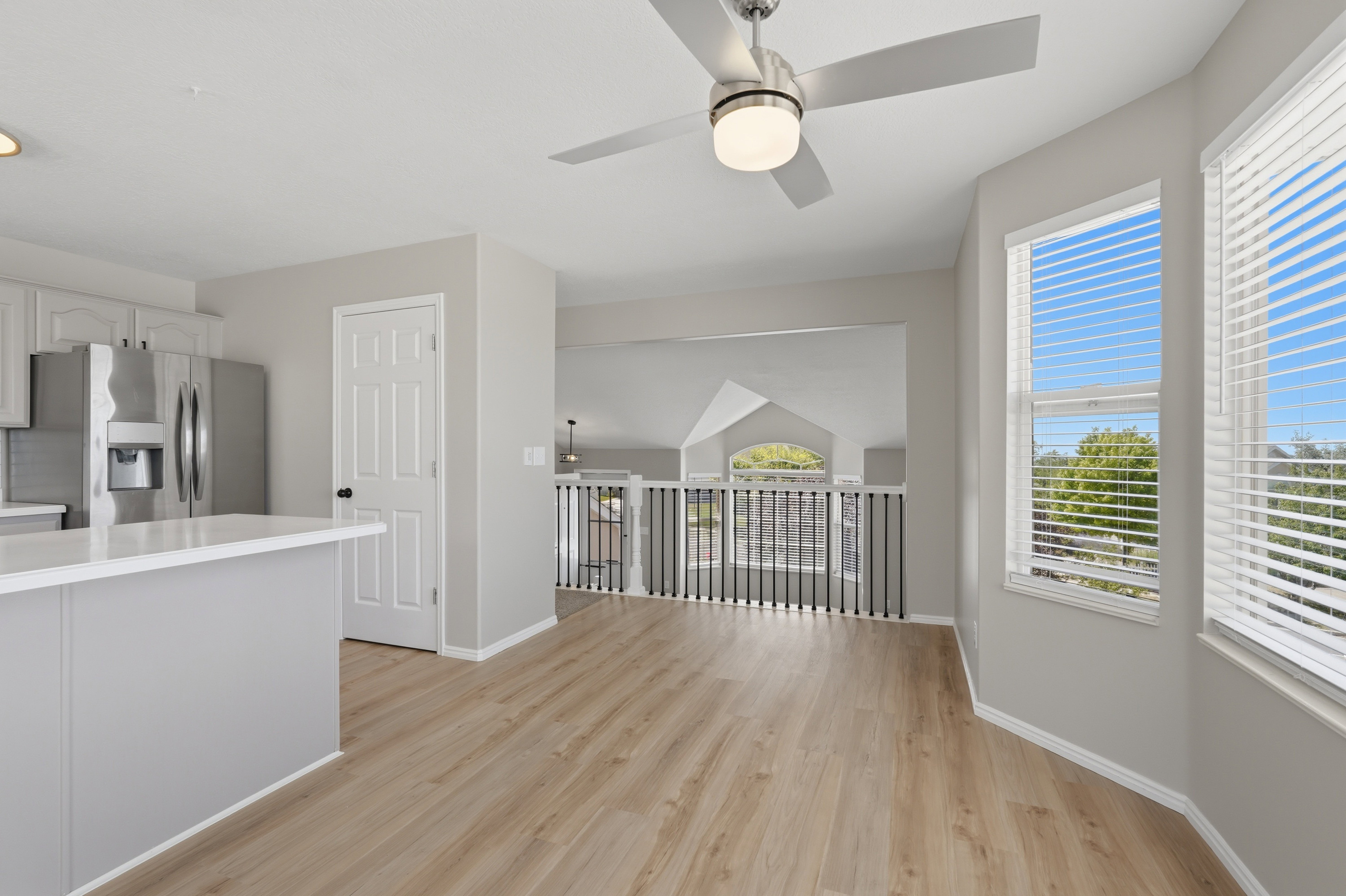 Open concept living area featuring wood-finish flooring, a contemporary ceiling fan, and large windows with horizontal blinds