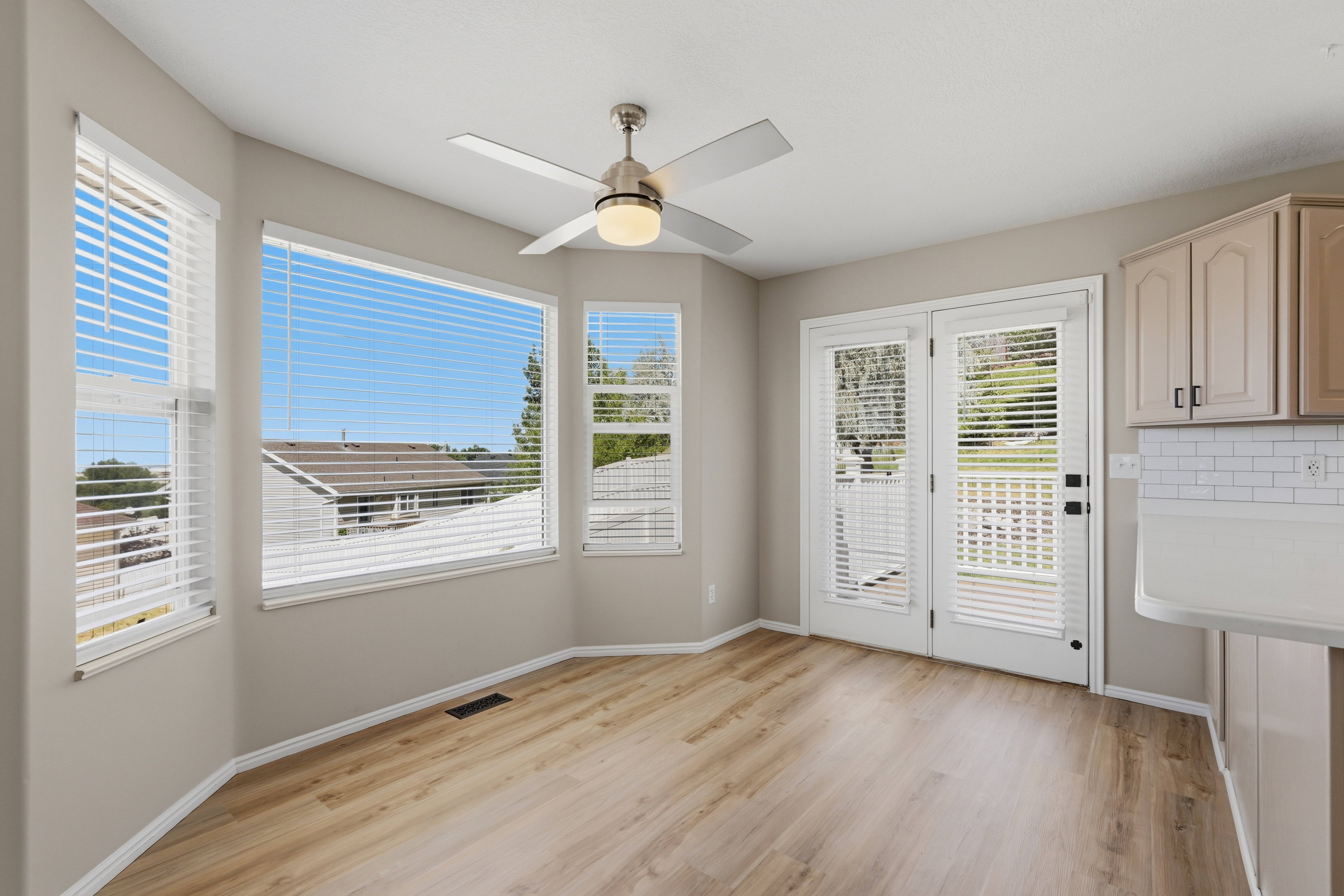 Bay window with multiple windows, wood-finish flooring, ceiling fan, and French doors leading to exterior decking
