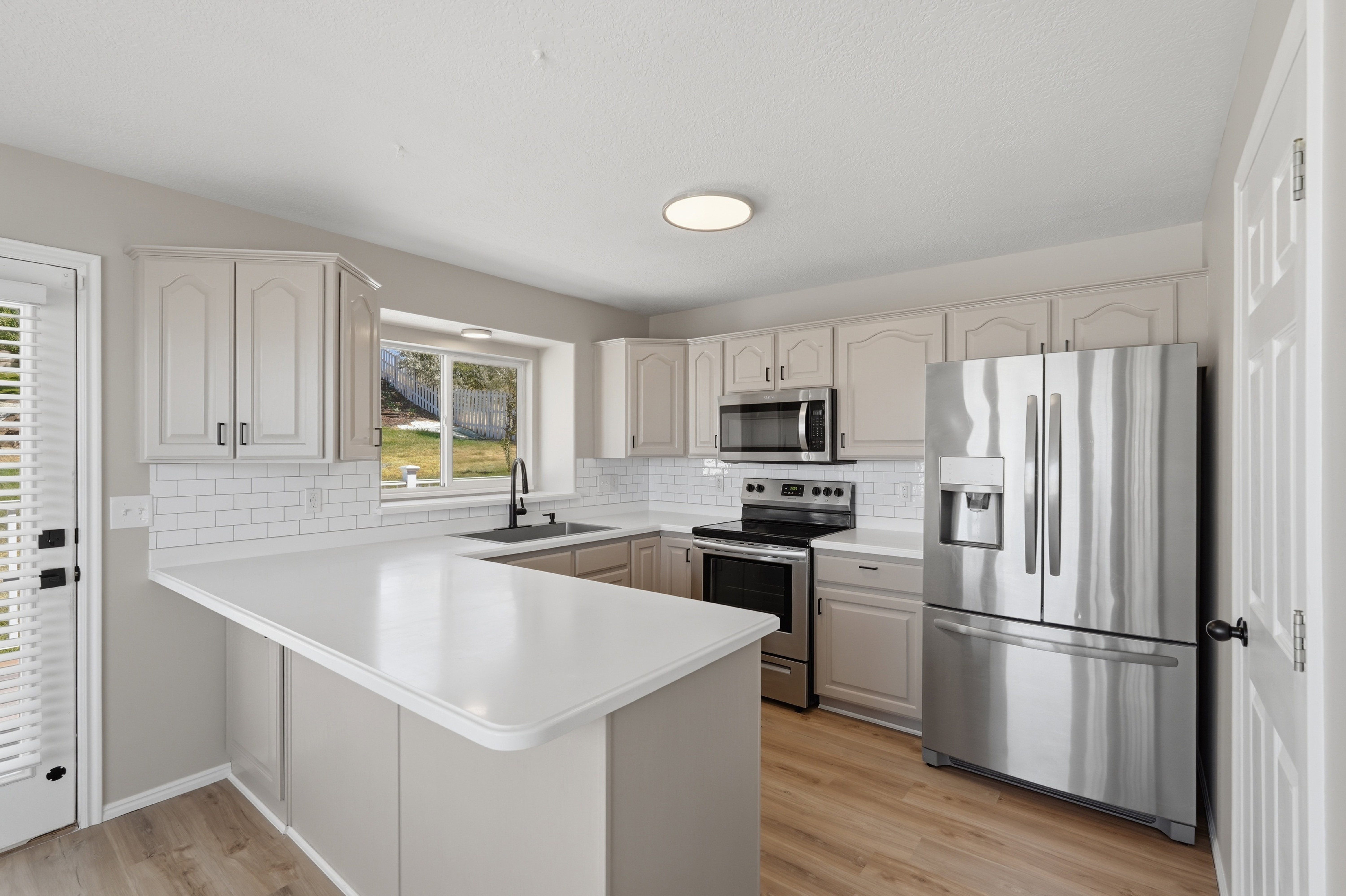 Kitchen featuring a U-shaped countertop with a breakfast bar, stainless steel appliances, a subway tile backsplash, light-toned cabinetry, and wood-finish flooring