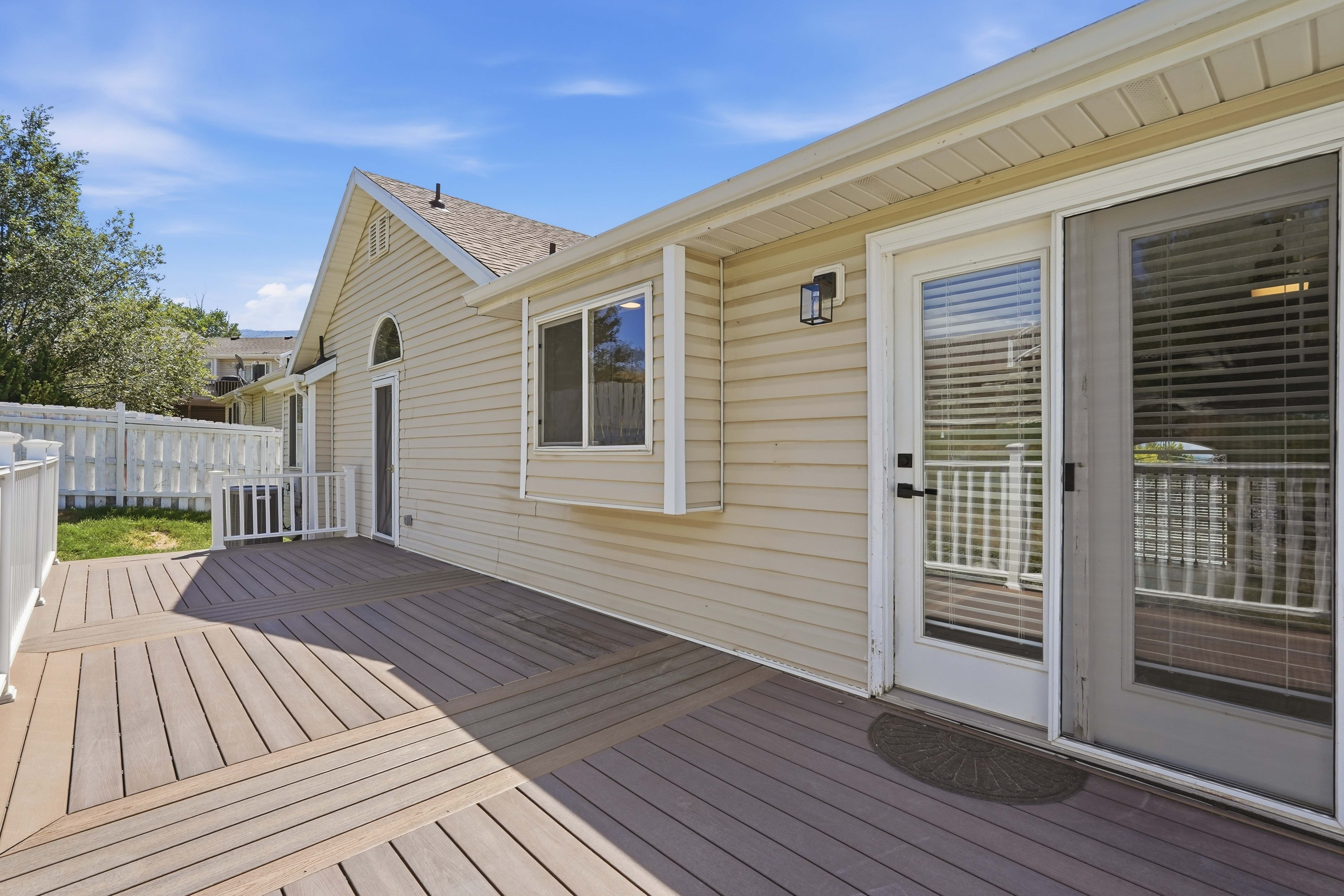 Spacious composite deck with a distinct geometric pattern, featuring a white picket fence, sliding glass door, and a bay window