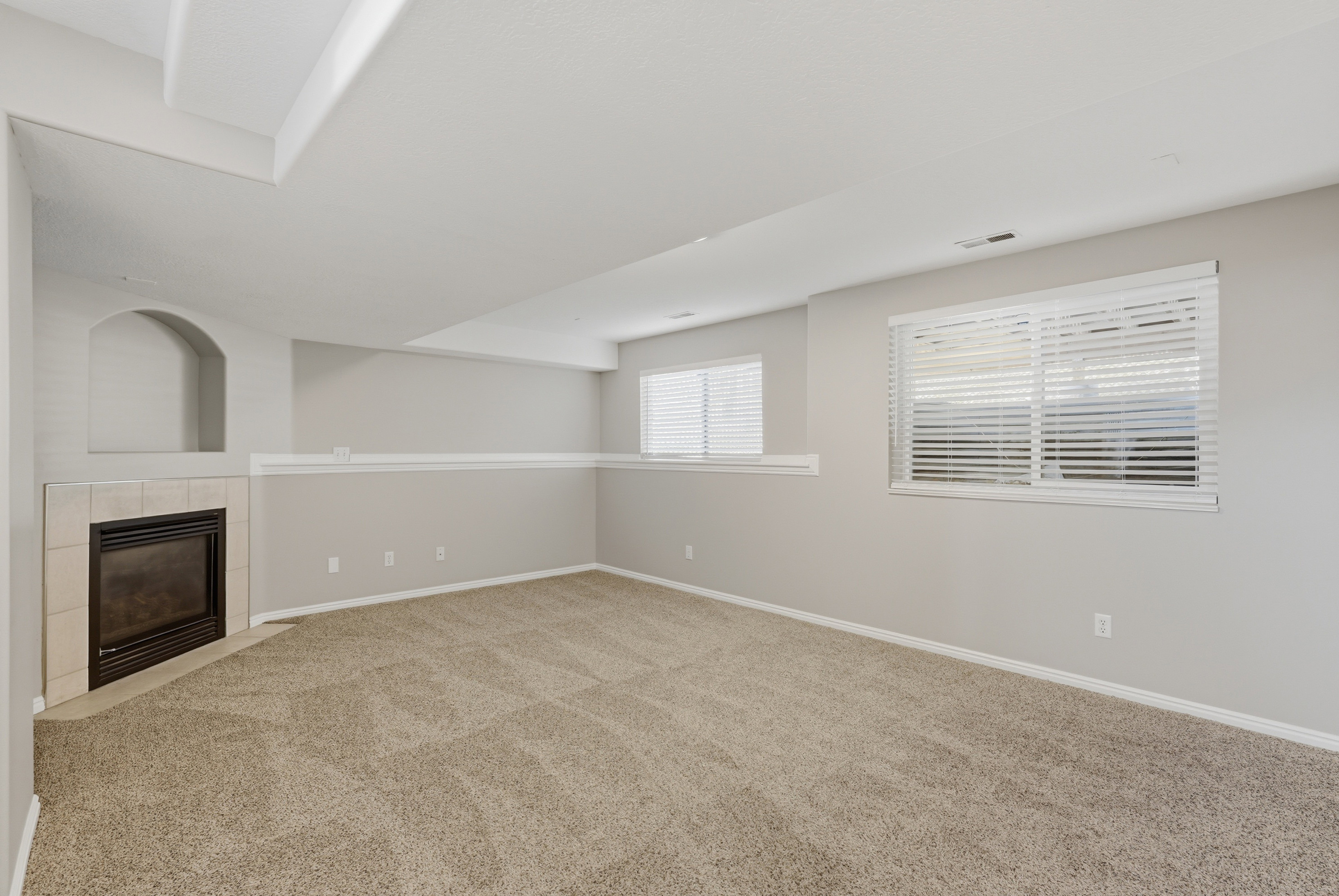 Carpeted room featuring a tiled fireplace with an arched niche, two windows with blinds, and recessed lighting